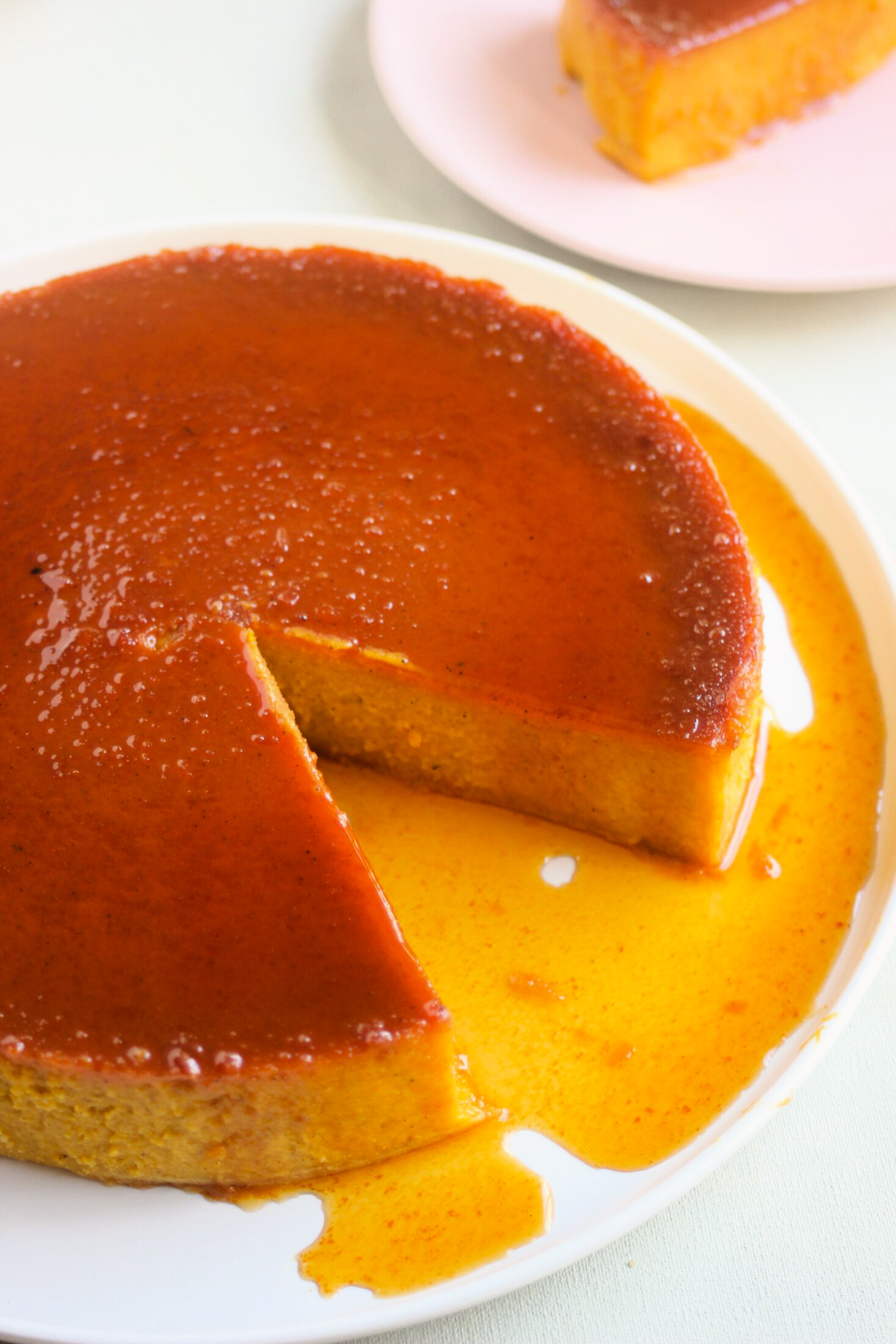 Pumpkin flan with caramel, without one portion, on a white plate.