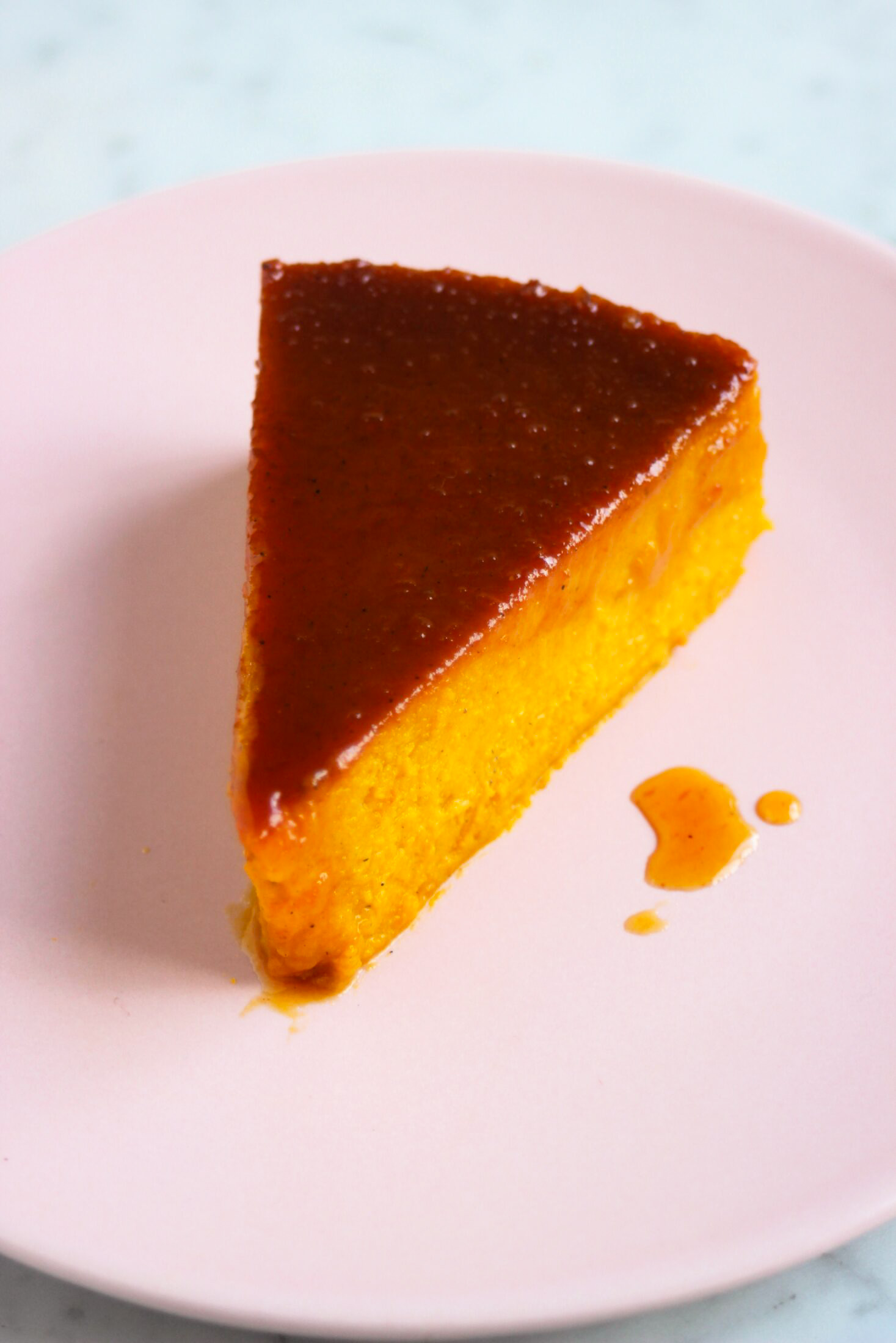 A portion of pumpkin flan with caramel on a pink plate.