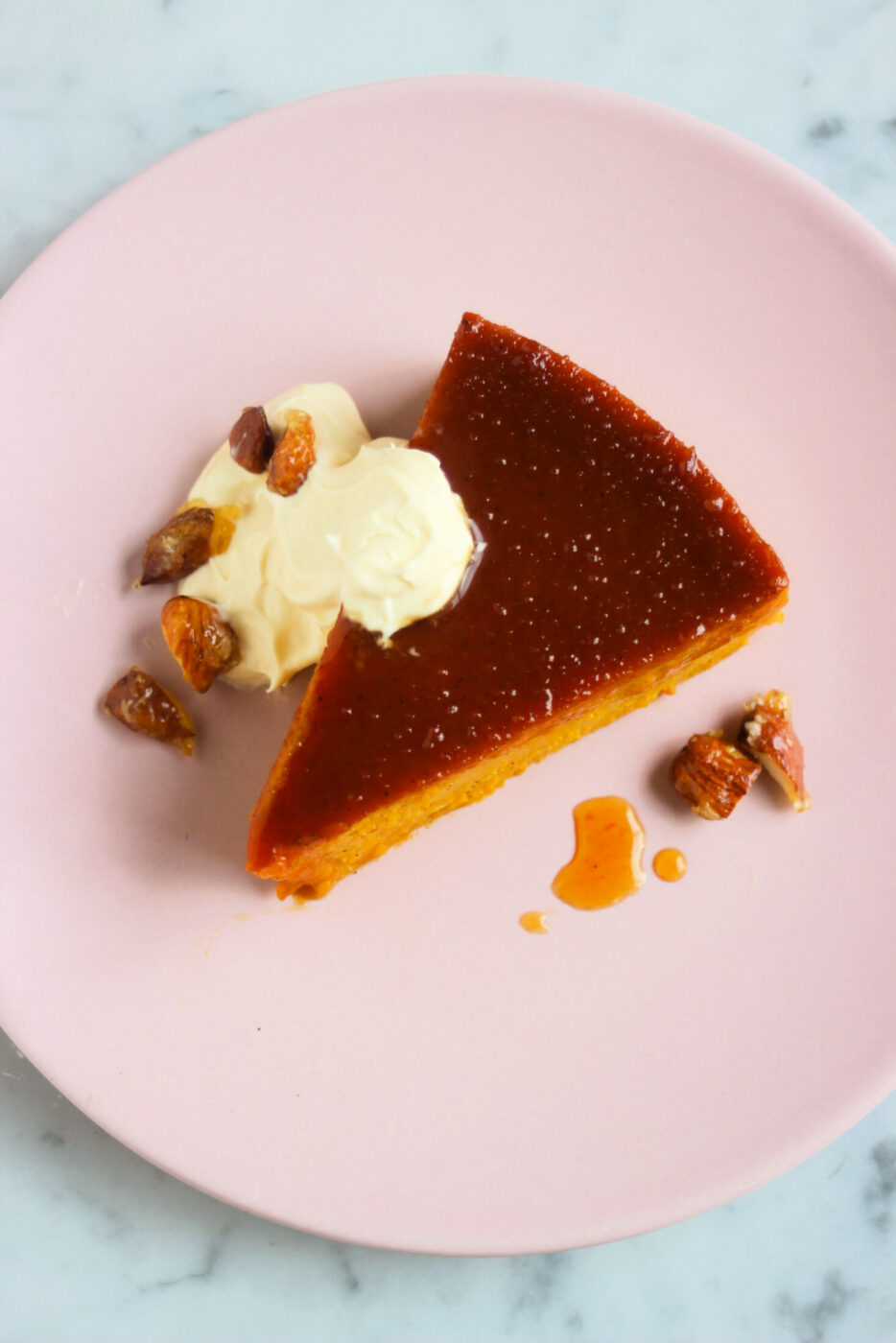 Top view of a pumpkin flan portion with whipped cream and caramelized almonds on a pink plate,