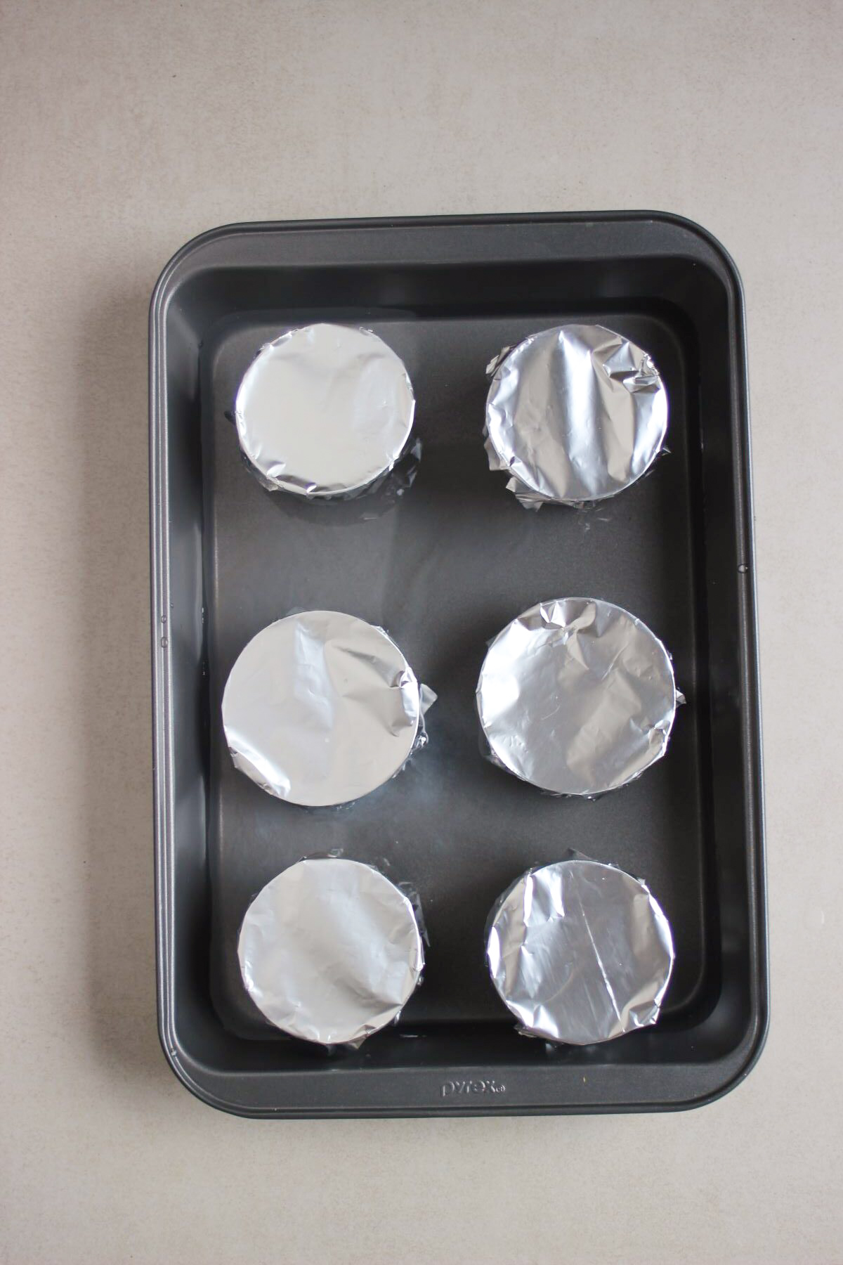 Baking sheet with individual flan molds covered with aluminum.
