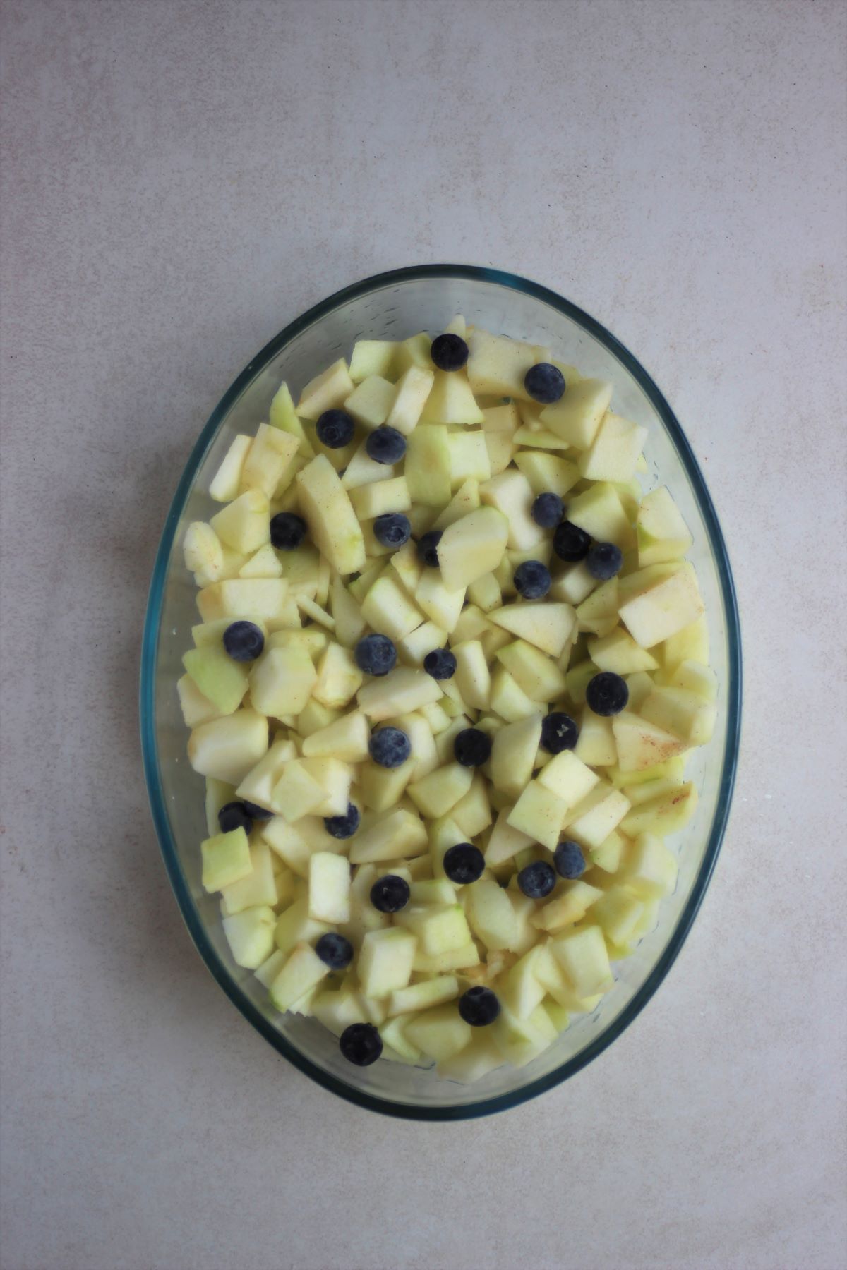 Oval baking dish with chopped and peel apples, and blueberries.