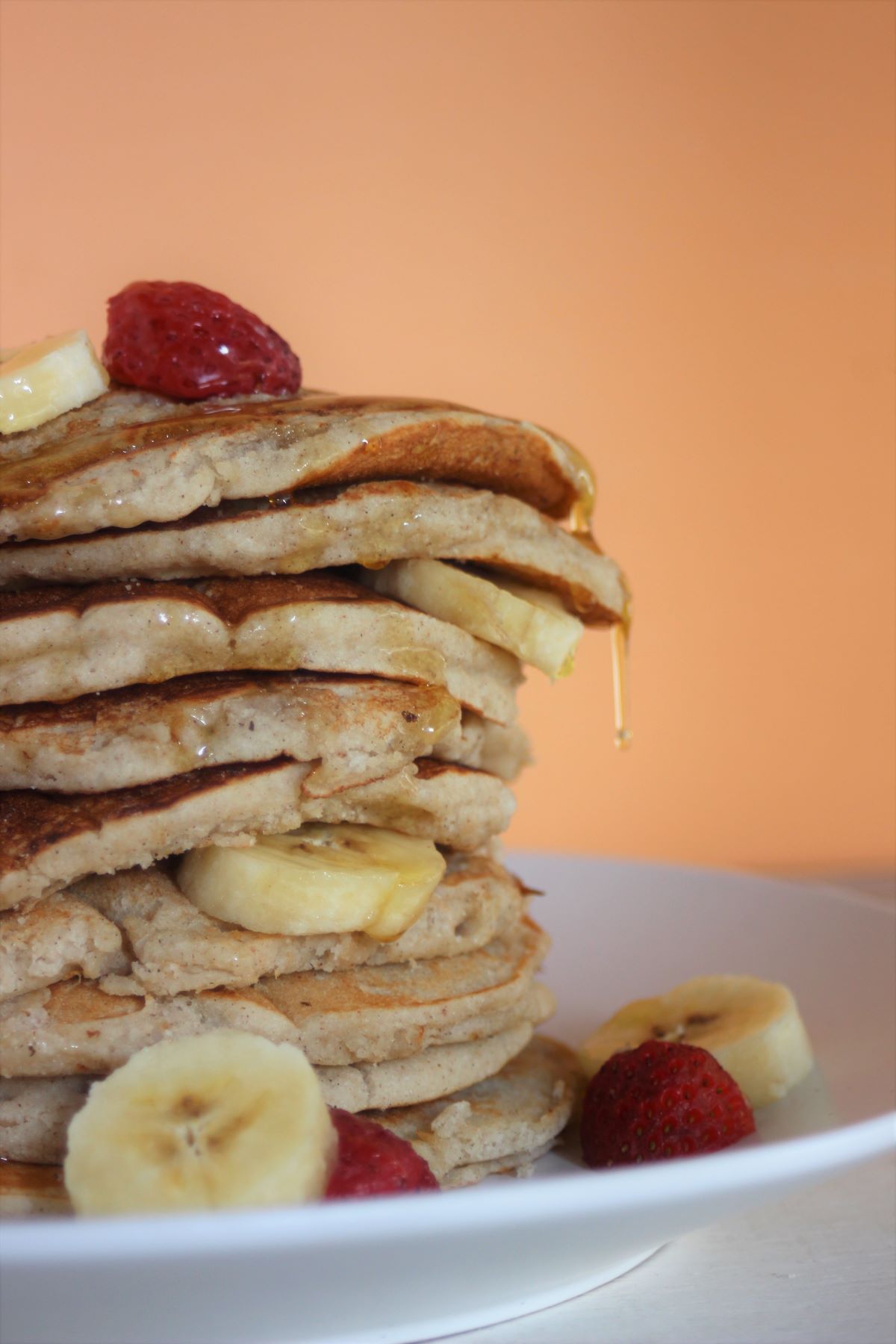 Tower of banana pancakes with banana slices and strawberries on a white plate seen from the front.
