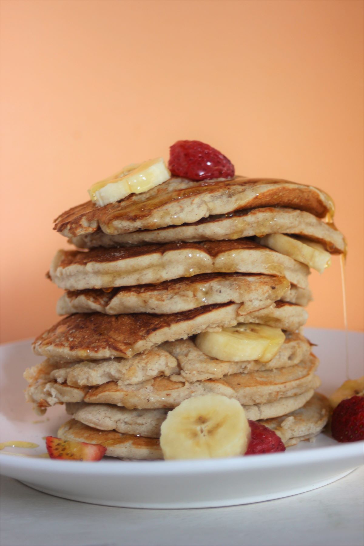 Tower of banana pancakes with banana slices and strawberries on a white plate.