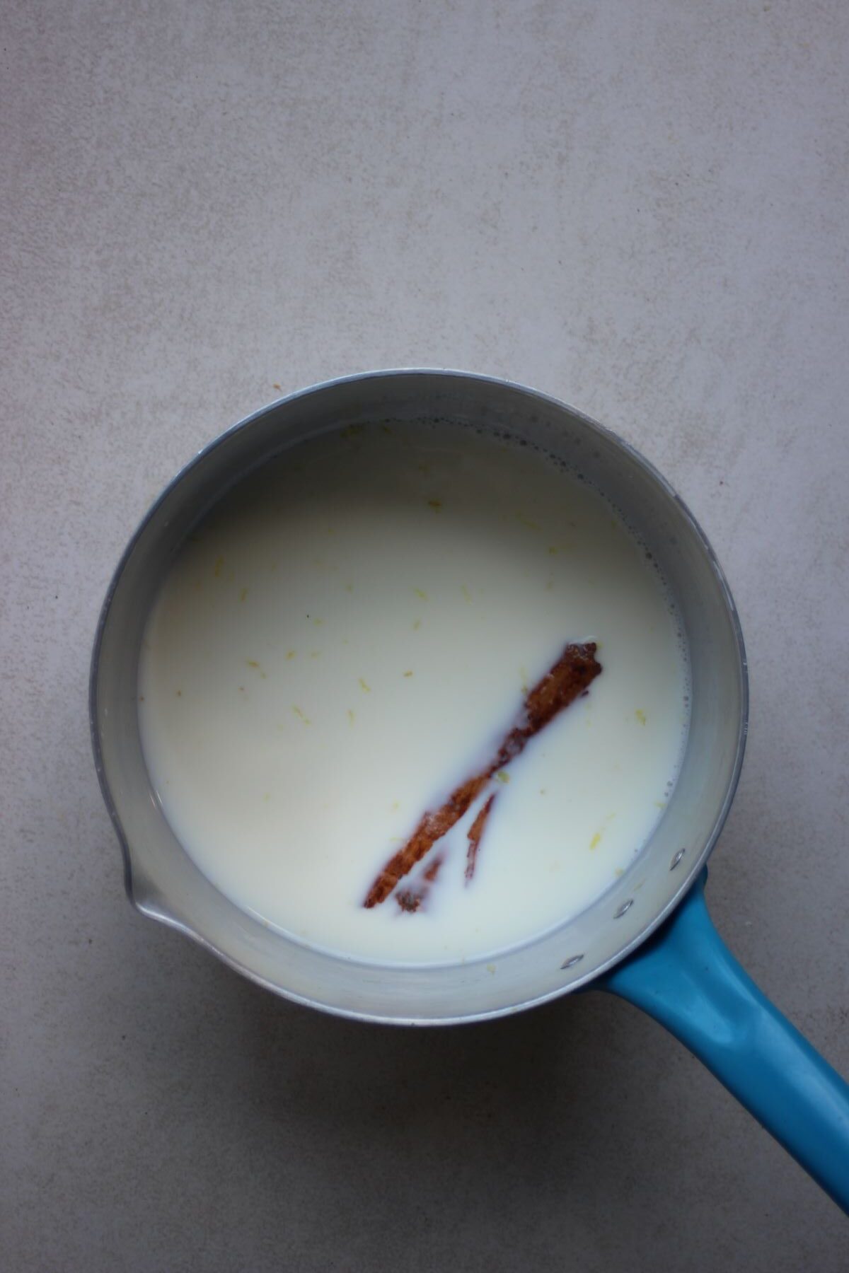 A deep saucepan with milk and a cinnamon stick on a white surface.