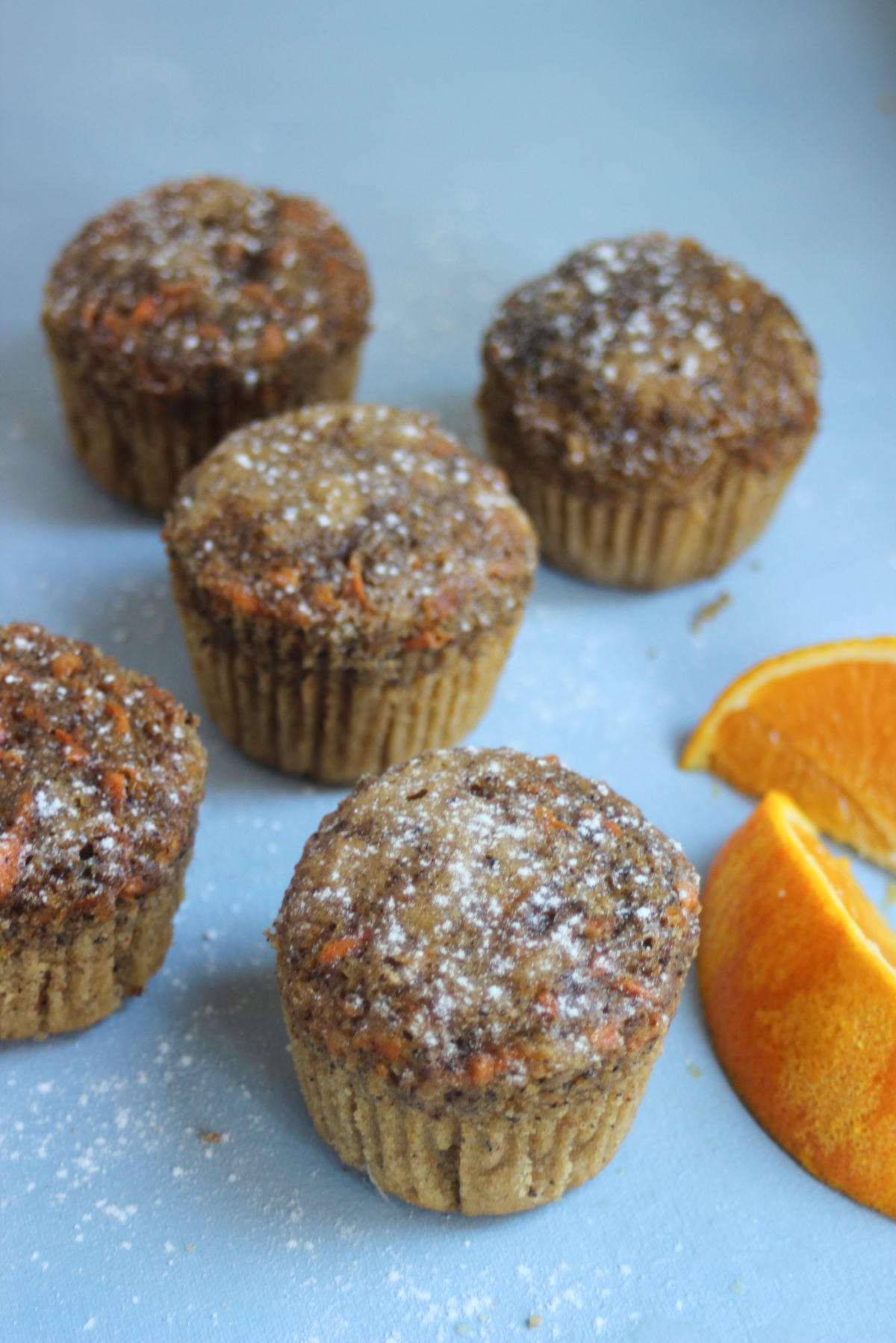 Carrot cake muffins, two orange slices, on a light blue surface.