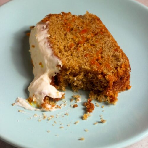 A slice of carrot loaf cake with cream cheese frosting on a light blue dish.