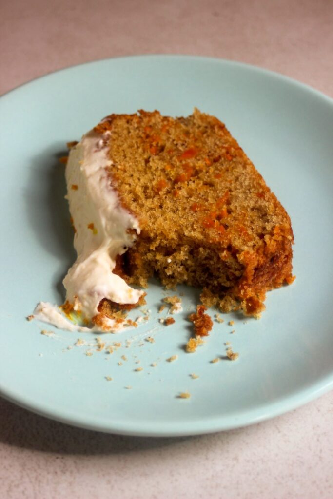 A slice of carrot loaf cake with cream cheese frosting on a light blue dish.