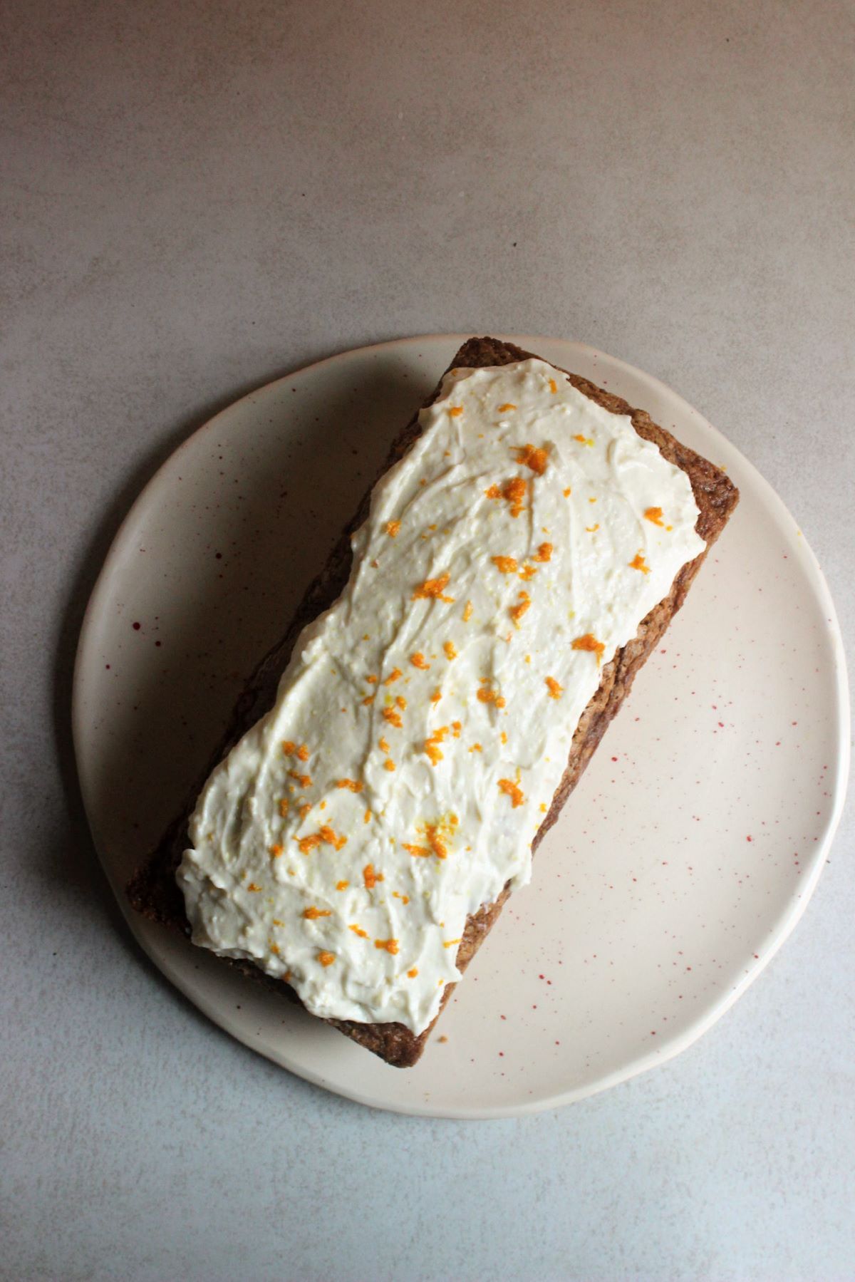 Carrot loaf cake with cream cheese frosting on a white plate seen from above.