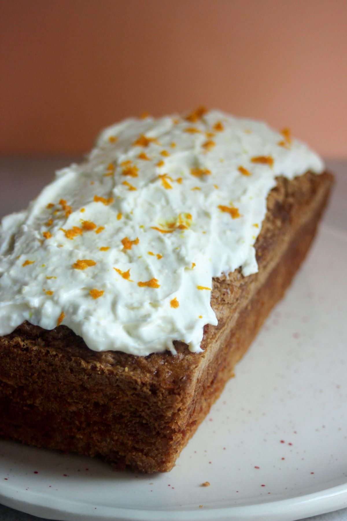 Carrot loaf cake with cream cheese frosting on a white plate.