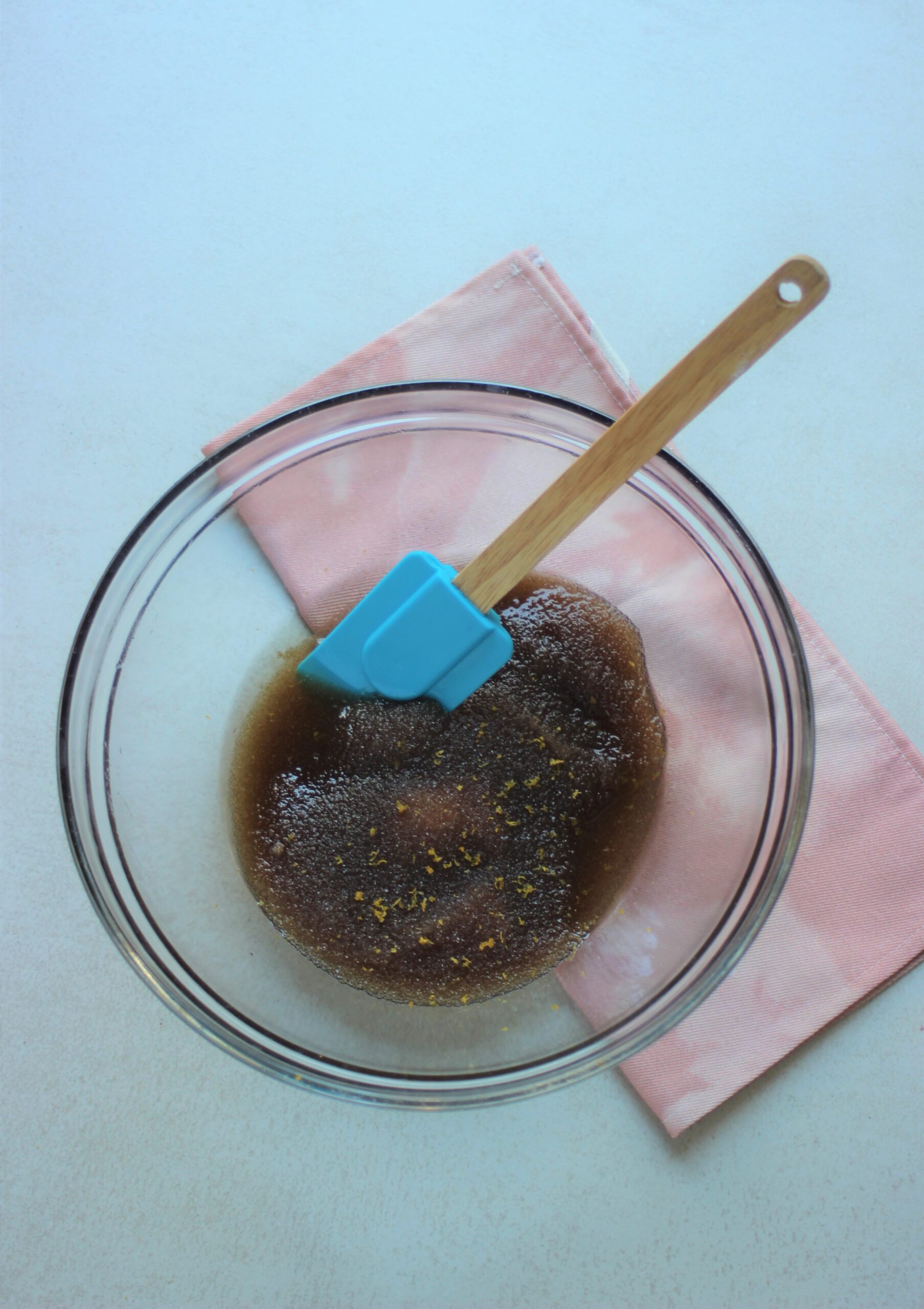 Glass bowl with a mixture of brown sugar and oil, and a rubber spatula. 