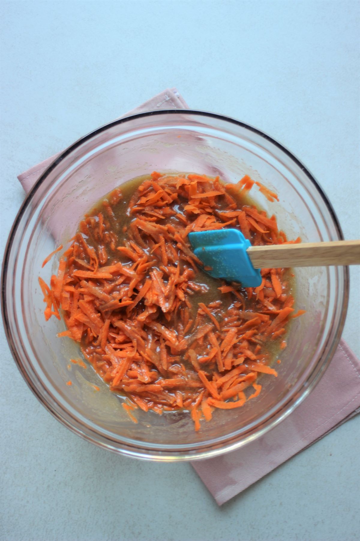 Glass bowl with a mixture with grated carrots and a rubber spatula.