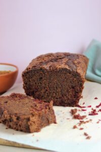 Beetroot chocolate loaf cake on parchment paper with a slice of it.