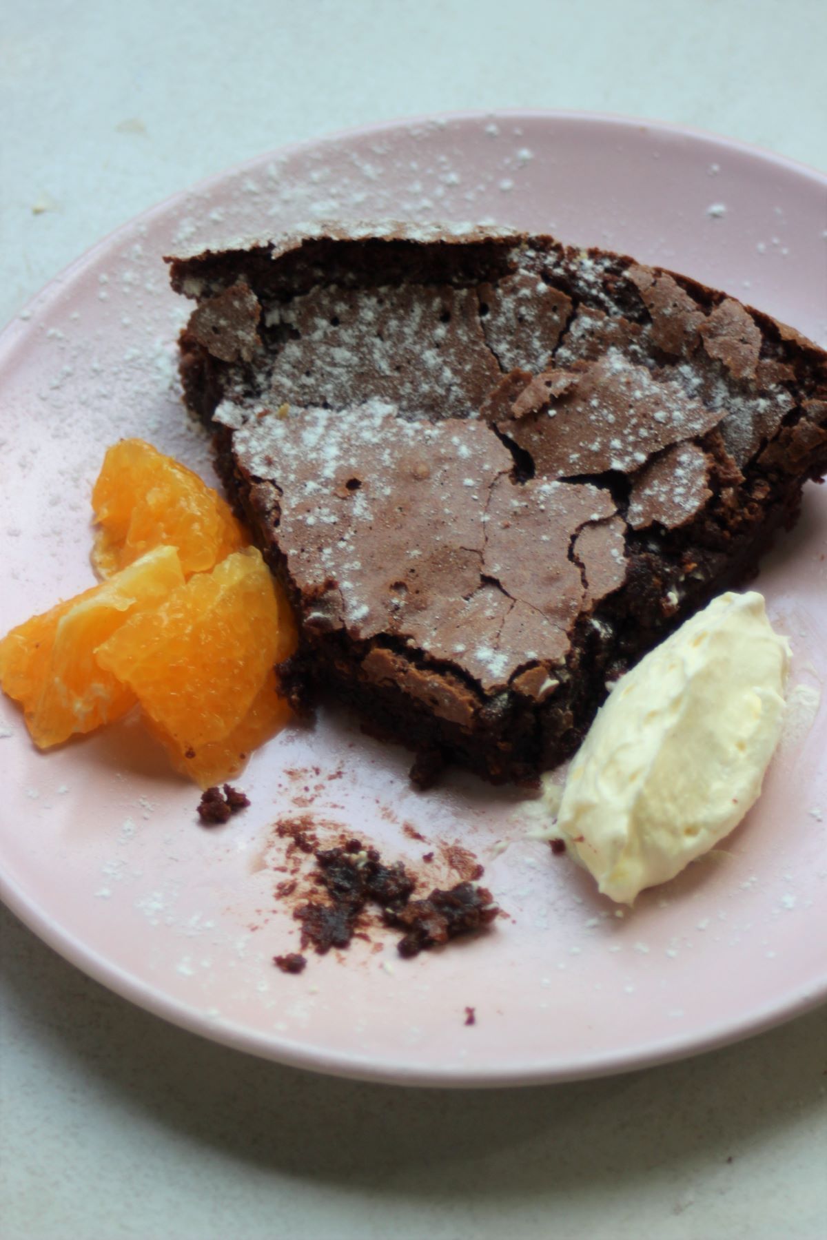Portion of chocolate cake, without a piece, with oranges slices and whipped cream on a pink plate.