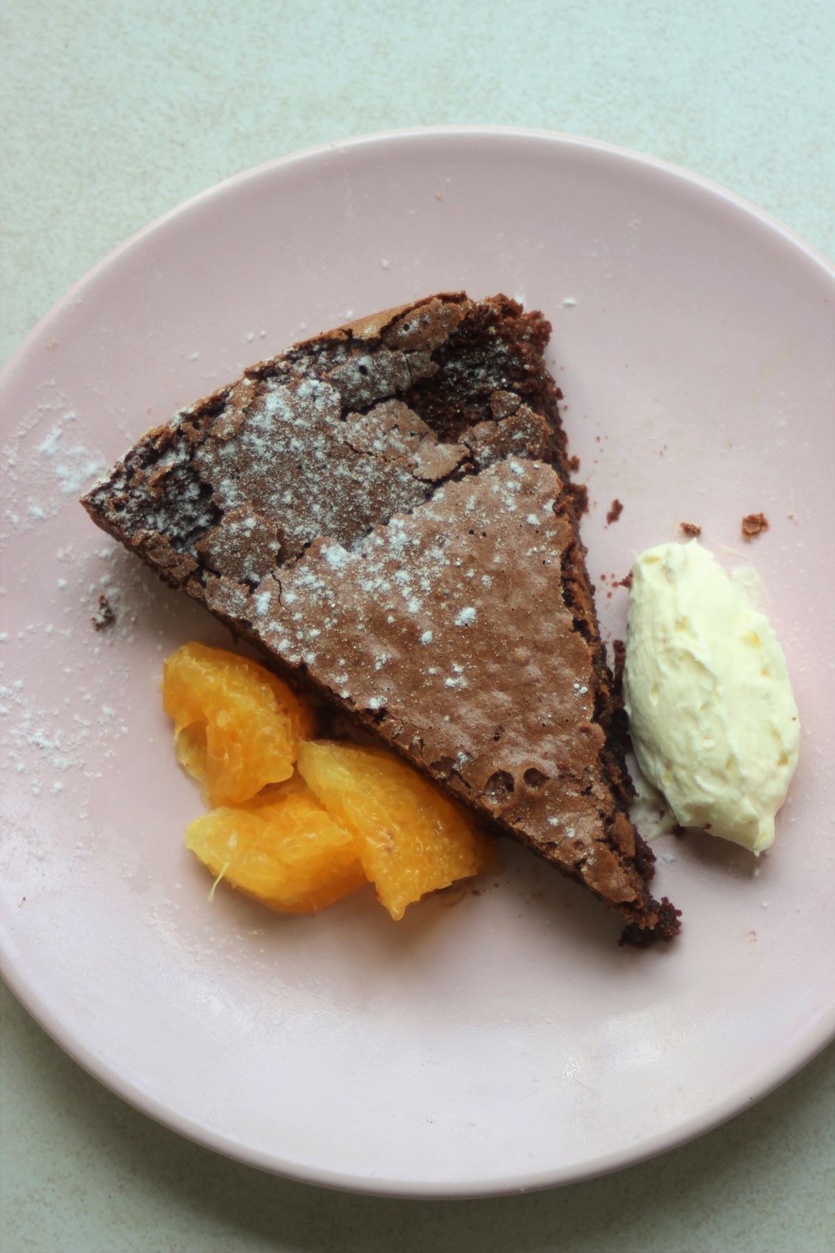 A portion of chocolate cake with oranges slices and whipped cream on a pink plate.