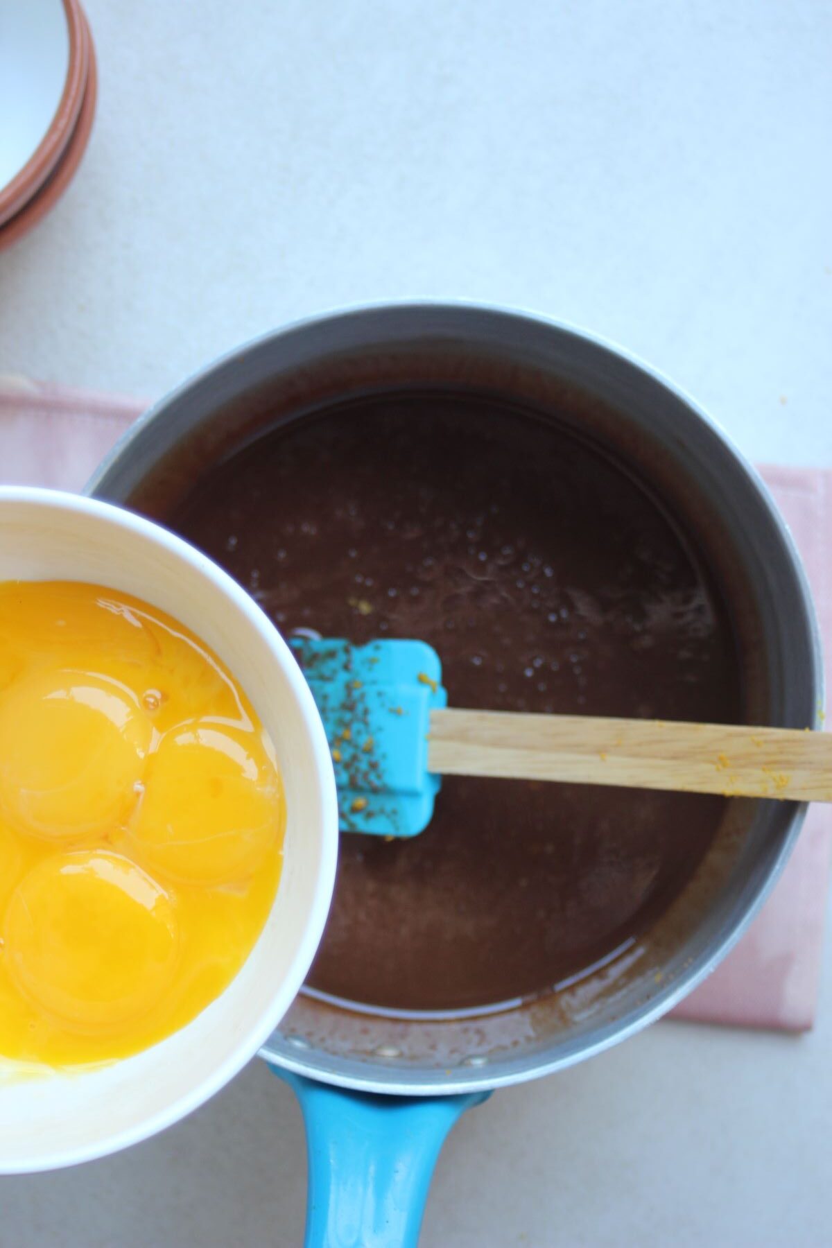 Bowl with egg yolks is about to be poured into a deep saucepan with melted chocolate.