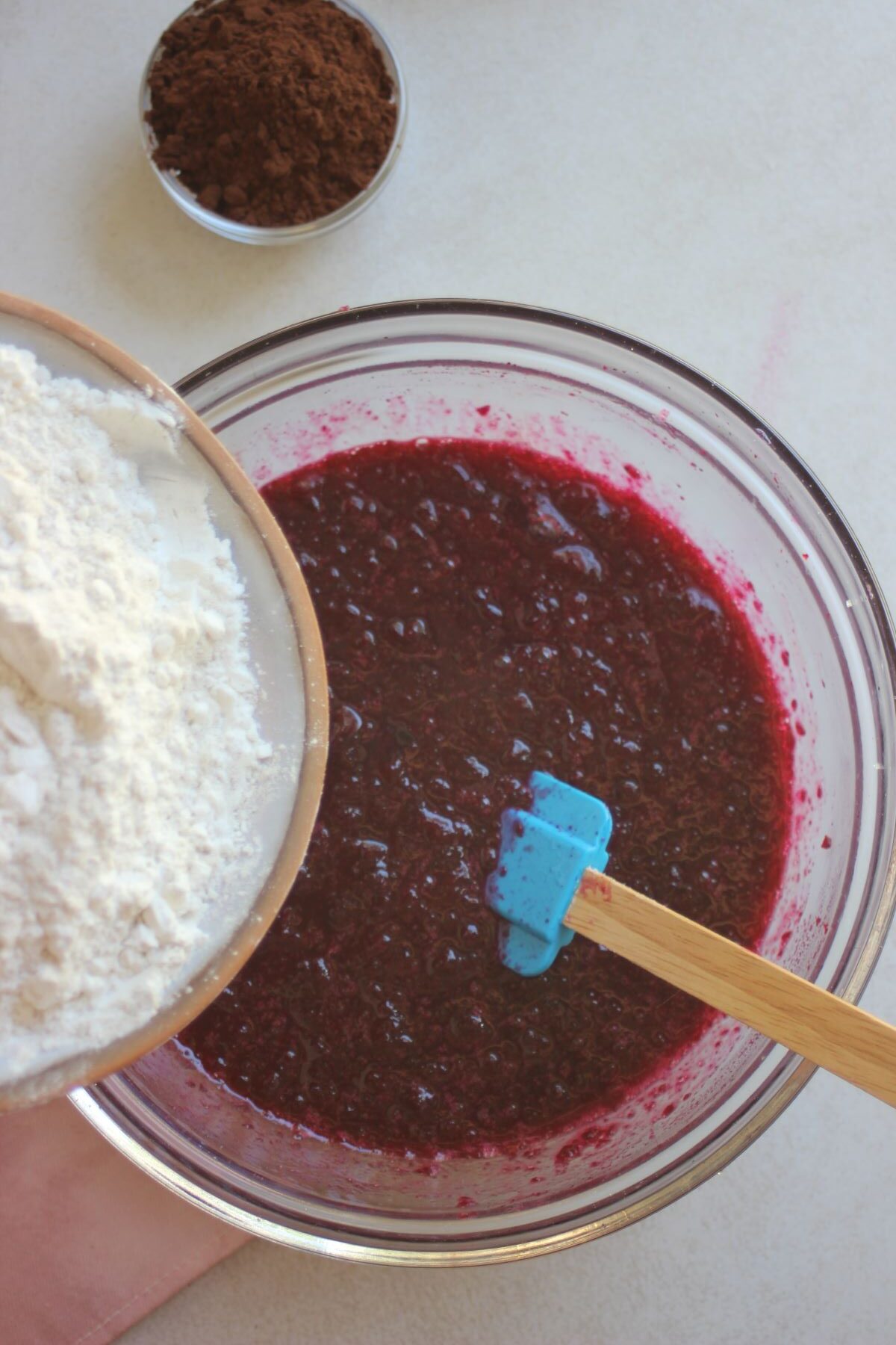 Plate with flour is about to be poured into a glass bowl with a red mixture.