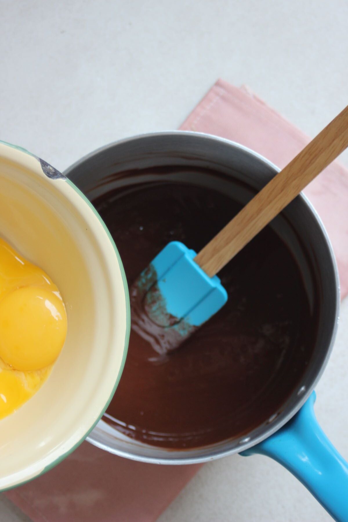 A bowl with egg yolks is about to be poured into a saucepan with melted chocolate.
