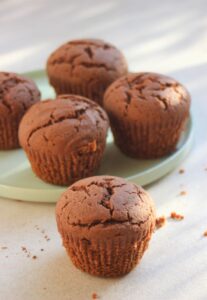 A chocolate muffin, and many muffins behind on a aqua green plate.