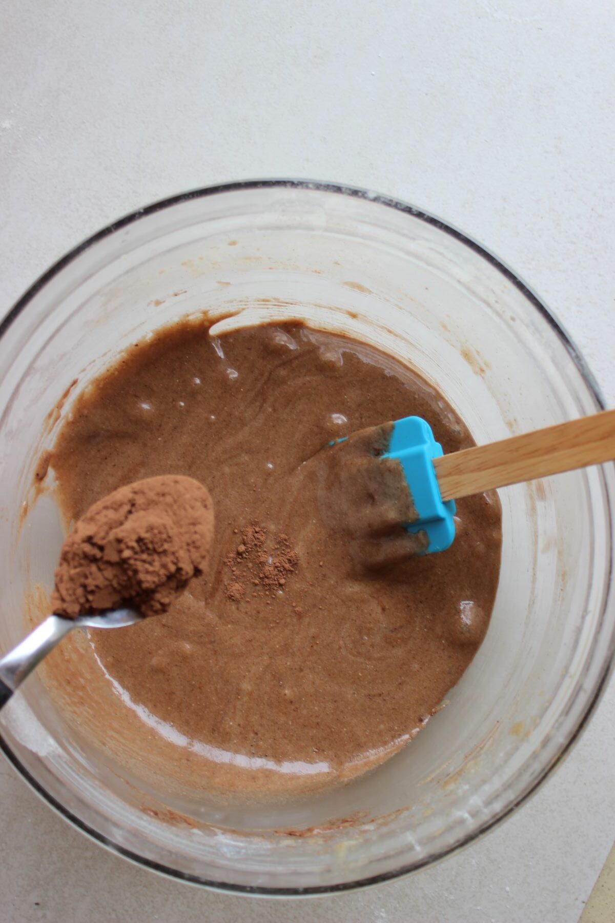 A spoon with cacao is about to be poured into a bowl with a brown mixture.