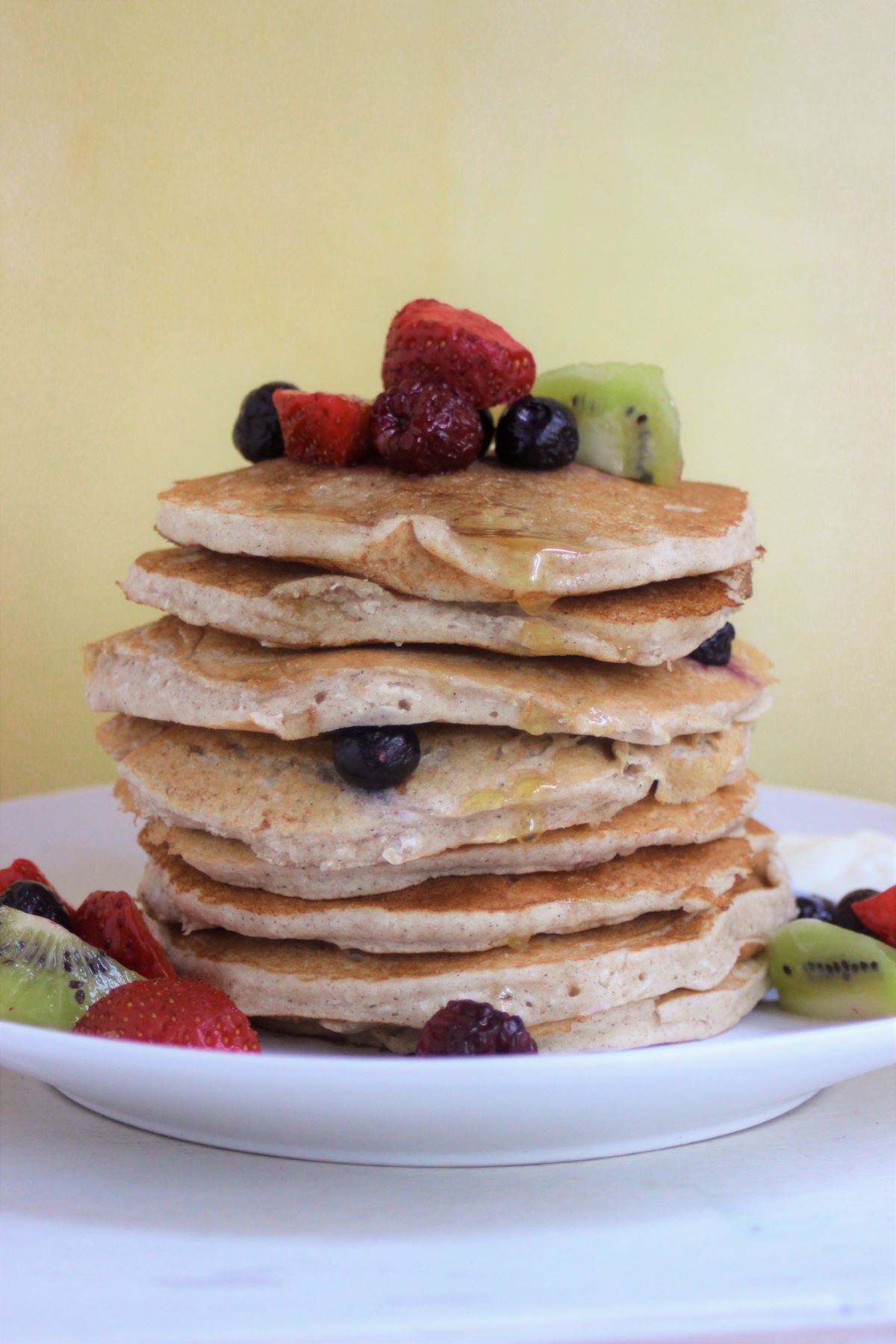 A tower of pancakes with strawberries, blueberries, and kiwis on a white dish.