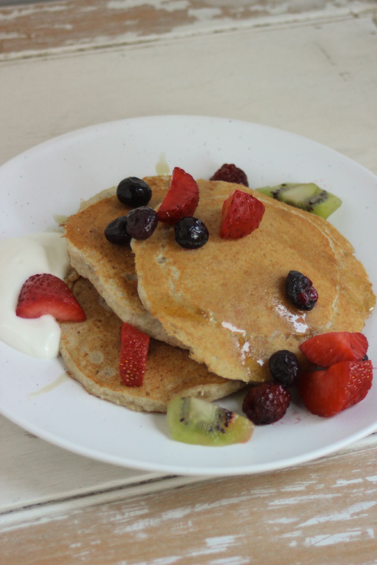 Coconut pancakes with berries, strawberries, and kiwis on a white plate.