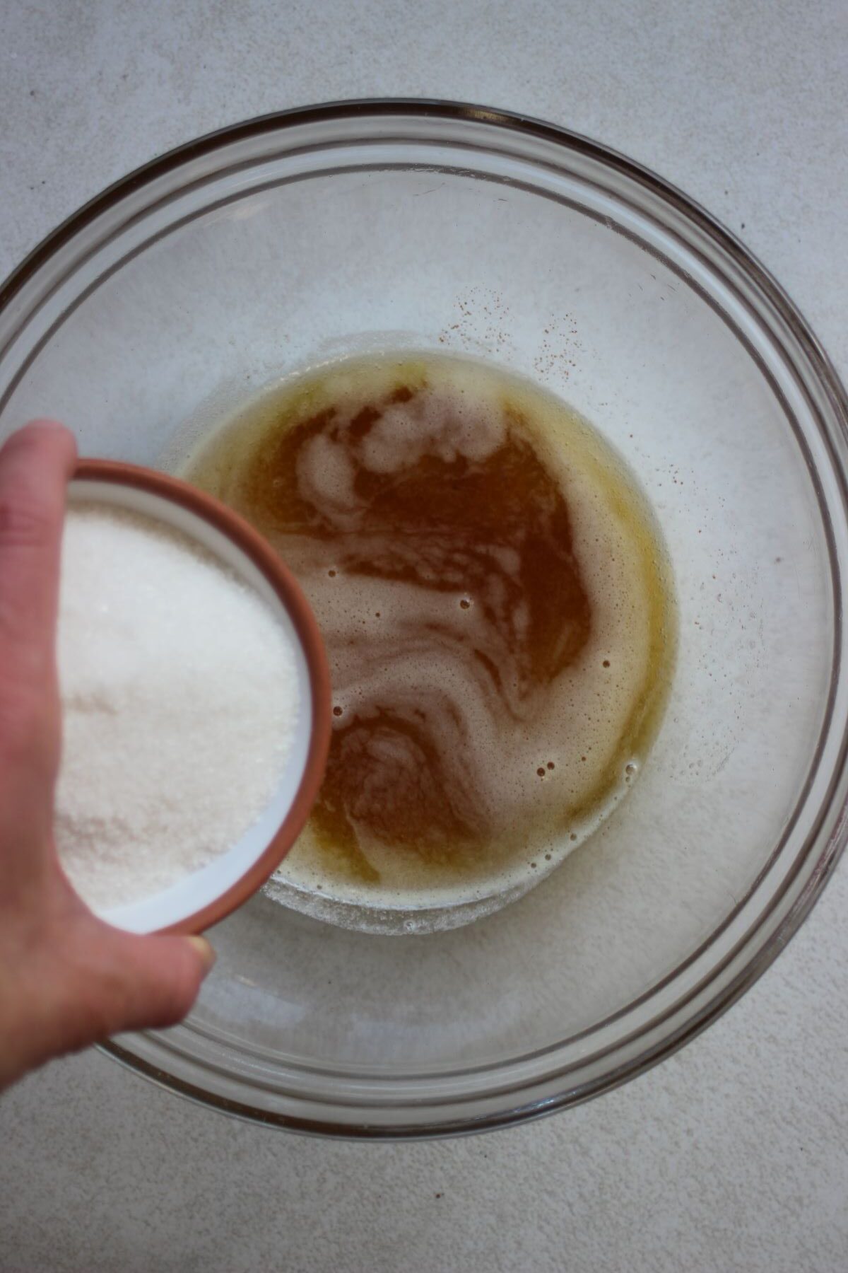 A bowl with sugar is about to be poured into a bowl with brown liquid.