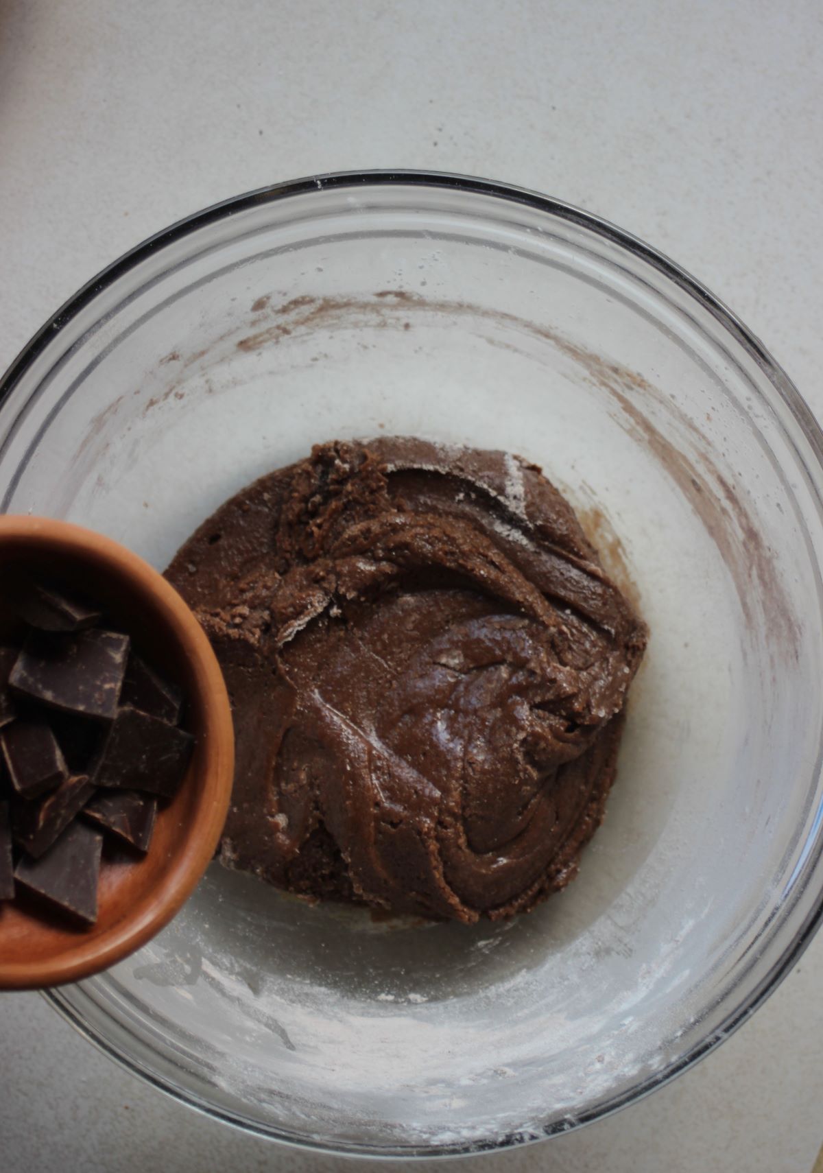 Bowl with chocolate chunks is about to be poured into a bowl with cookie dough.