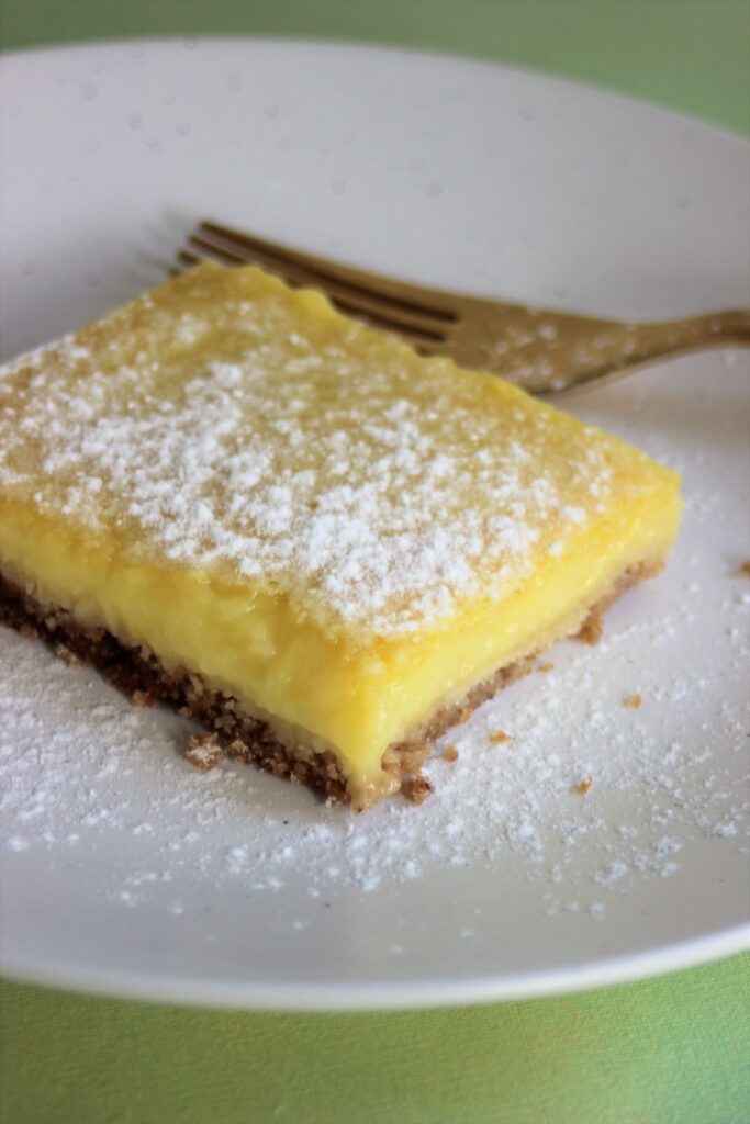 Lemon bar sprinkled with powdered sugar on a white plate.