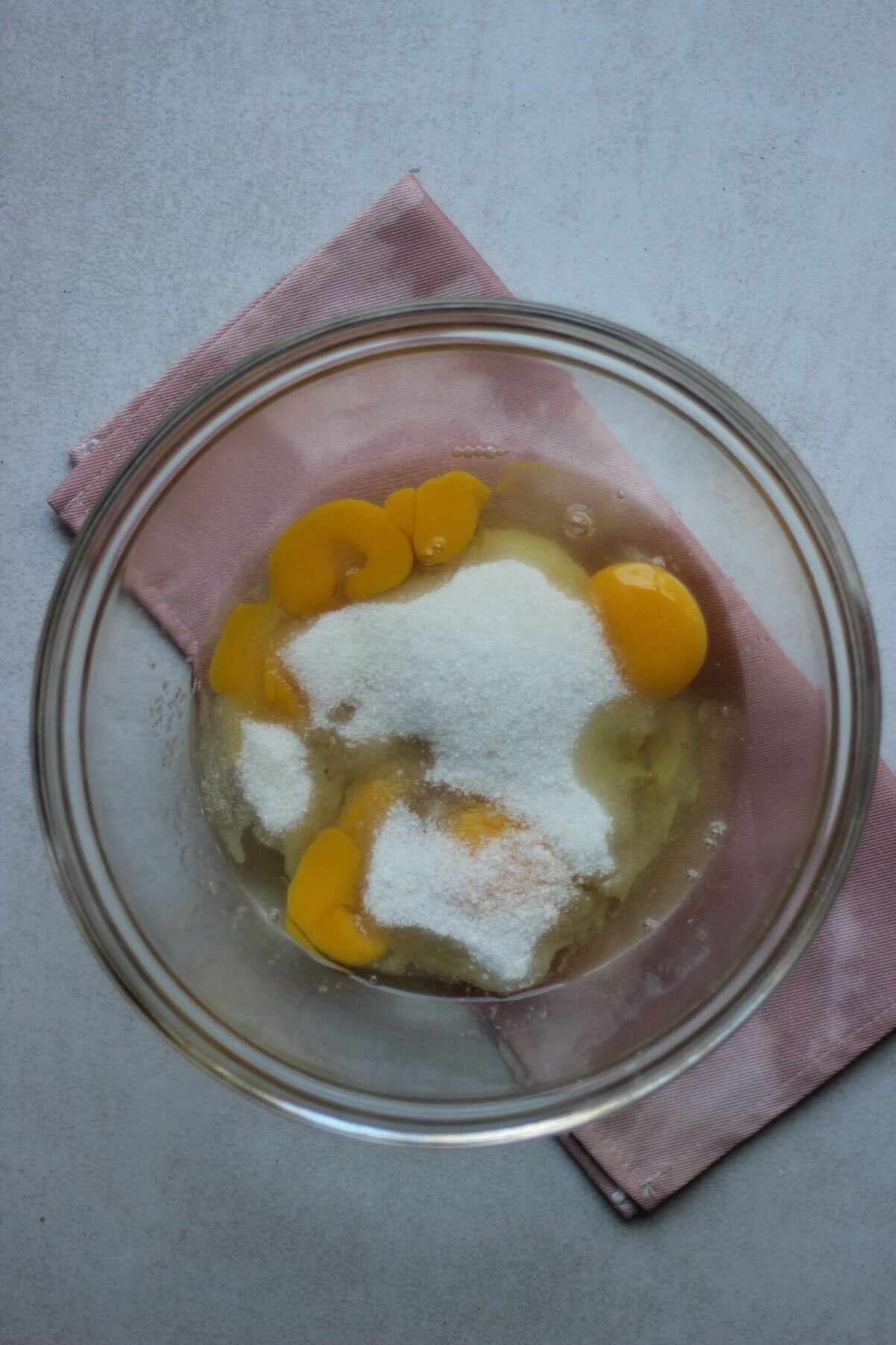 Glass bowl with egg and white yolks, and sugar. Pink napkin under the bowl.