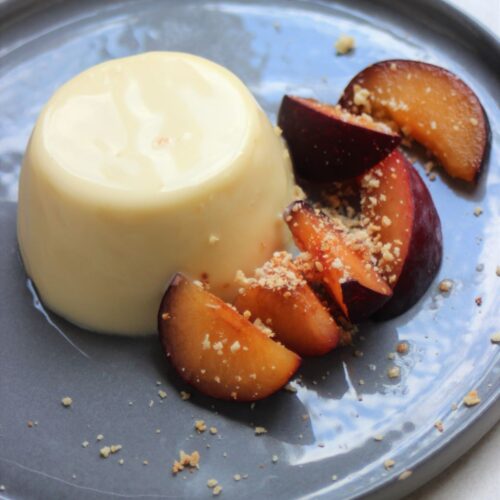 Panna Cotta and slices of plum on a grey plate.