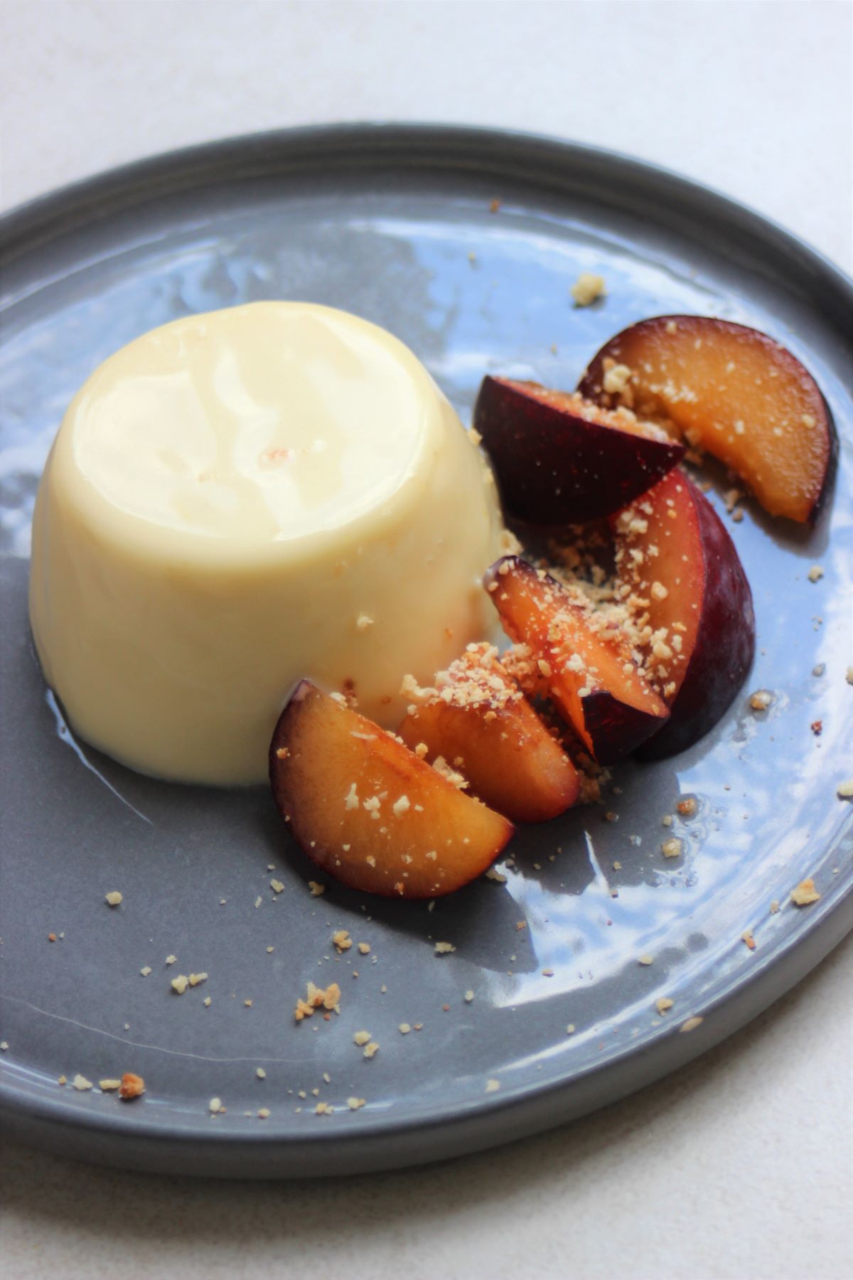 Panna Cotta and slices of plum on a grey plate.