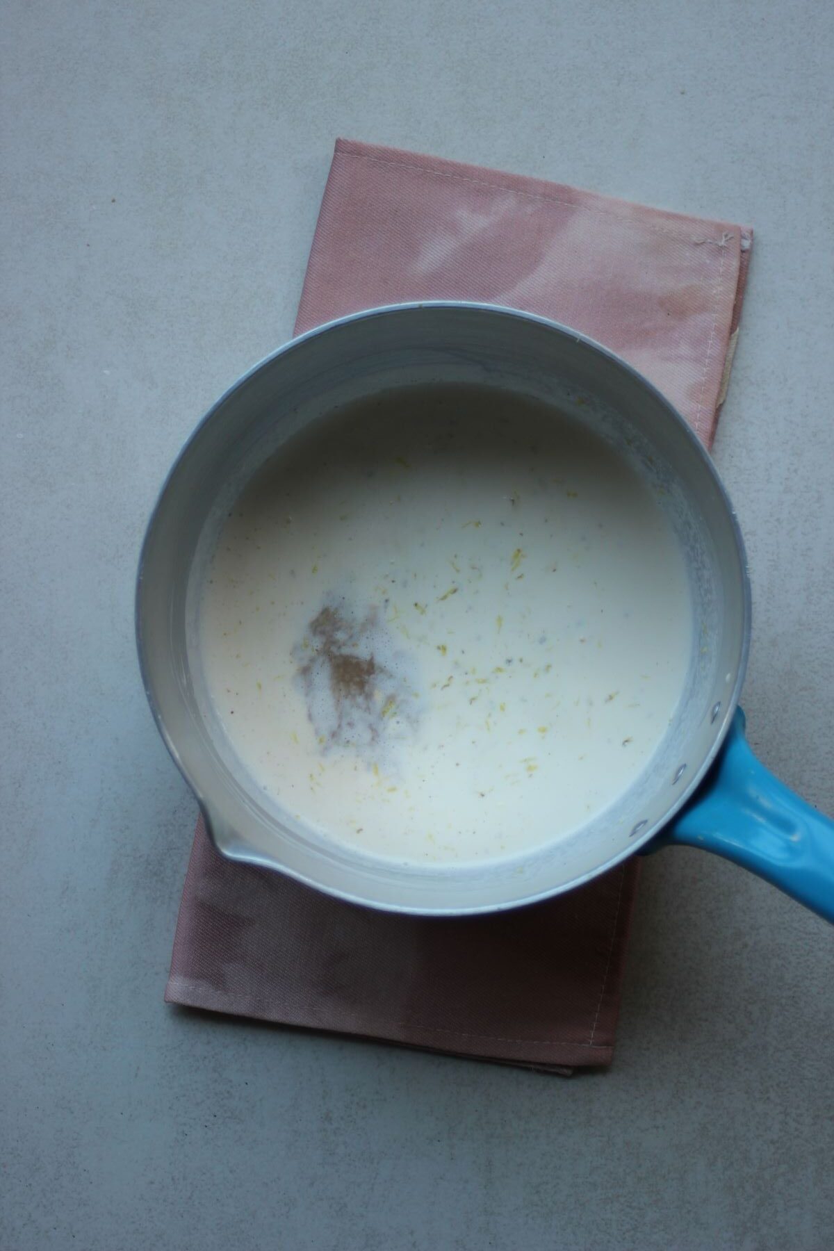 A deep saucepan with a white liquid and lemon zest.