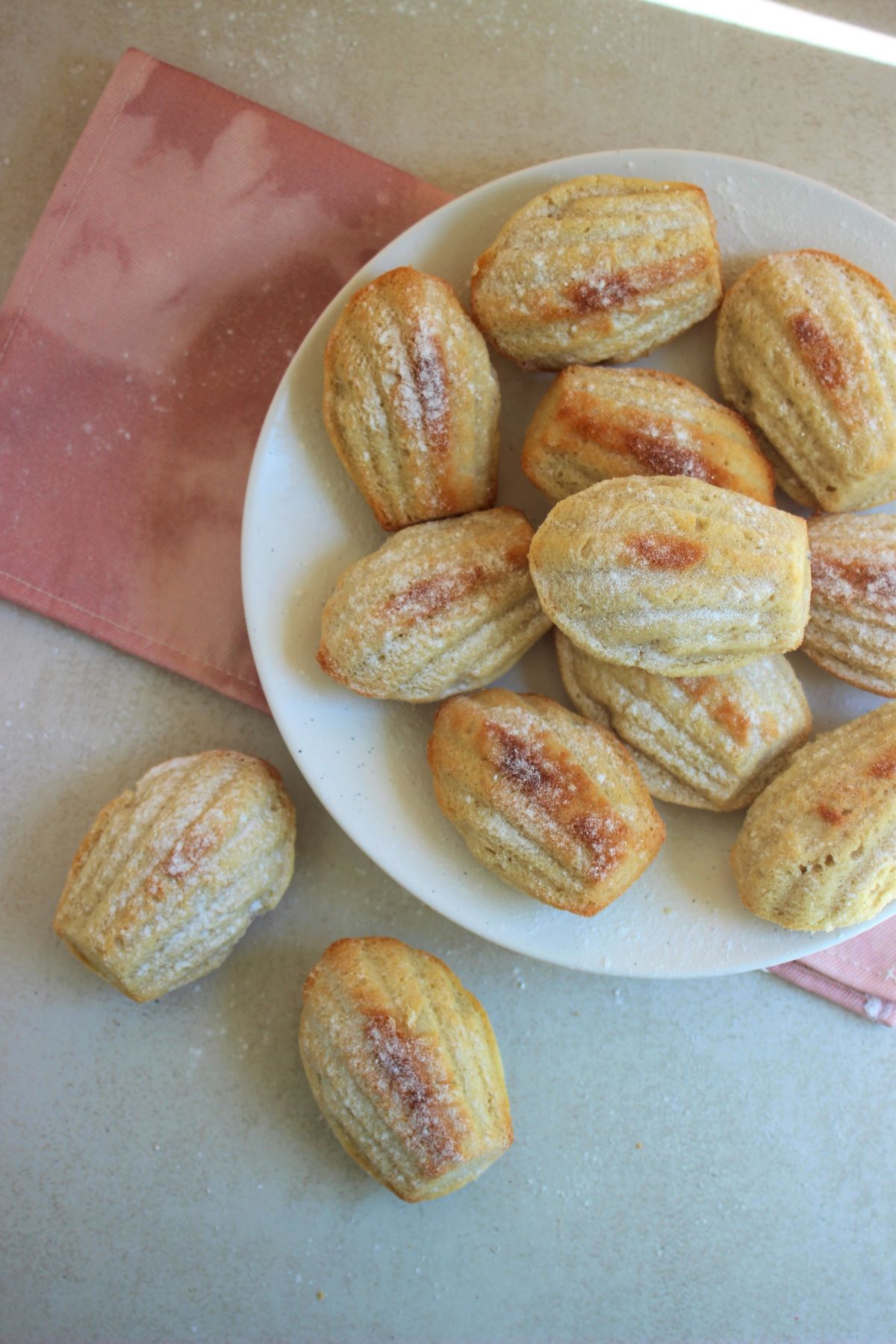 Many madeleines in a white plate, and two madeleines on the side seem from above.