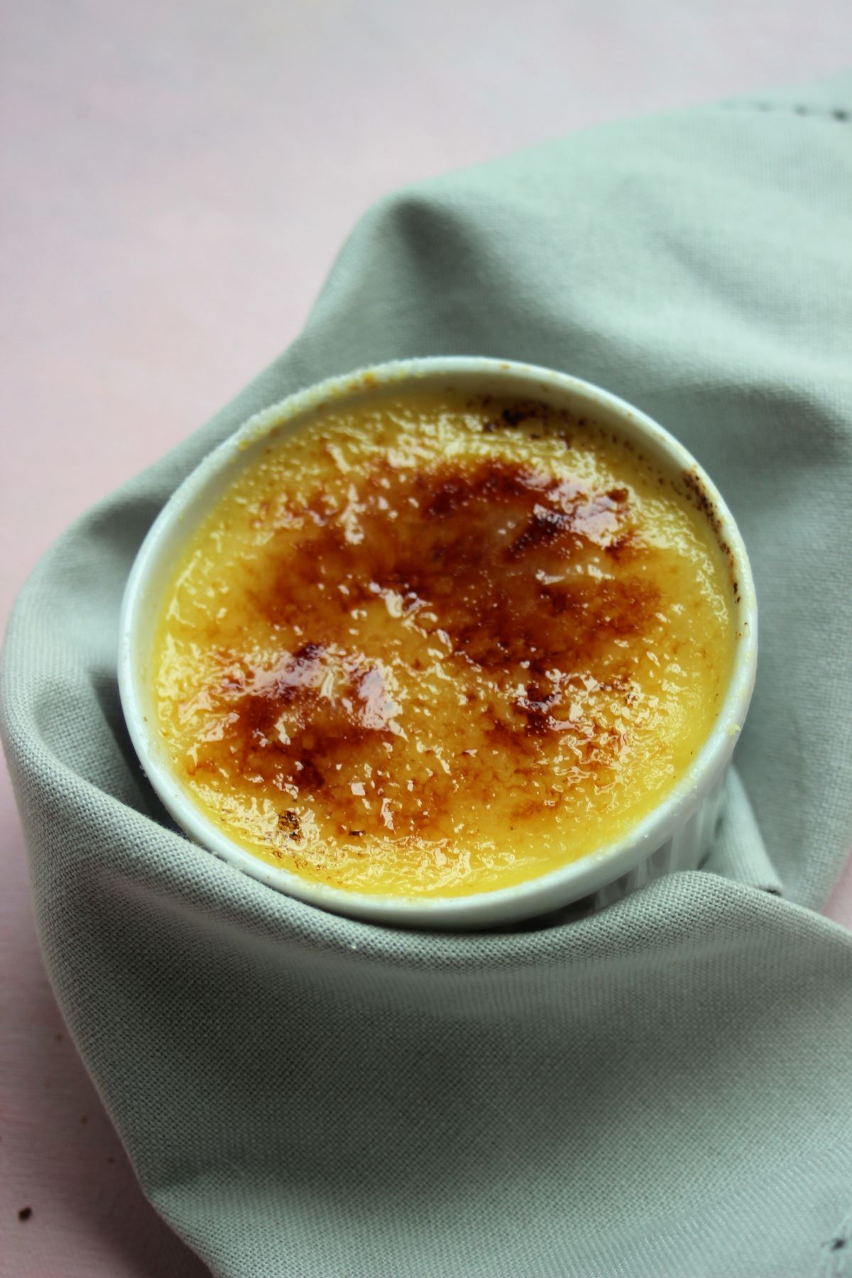 White ramekin with creme brulee wrapped in a napkin.