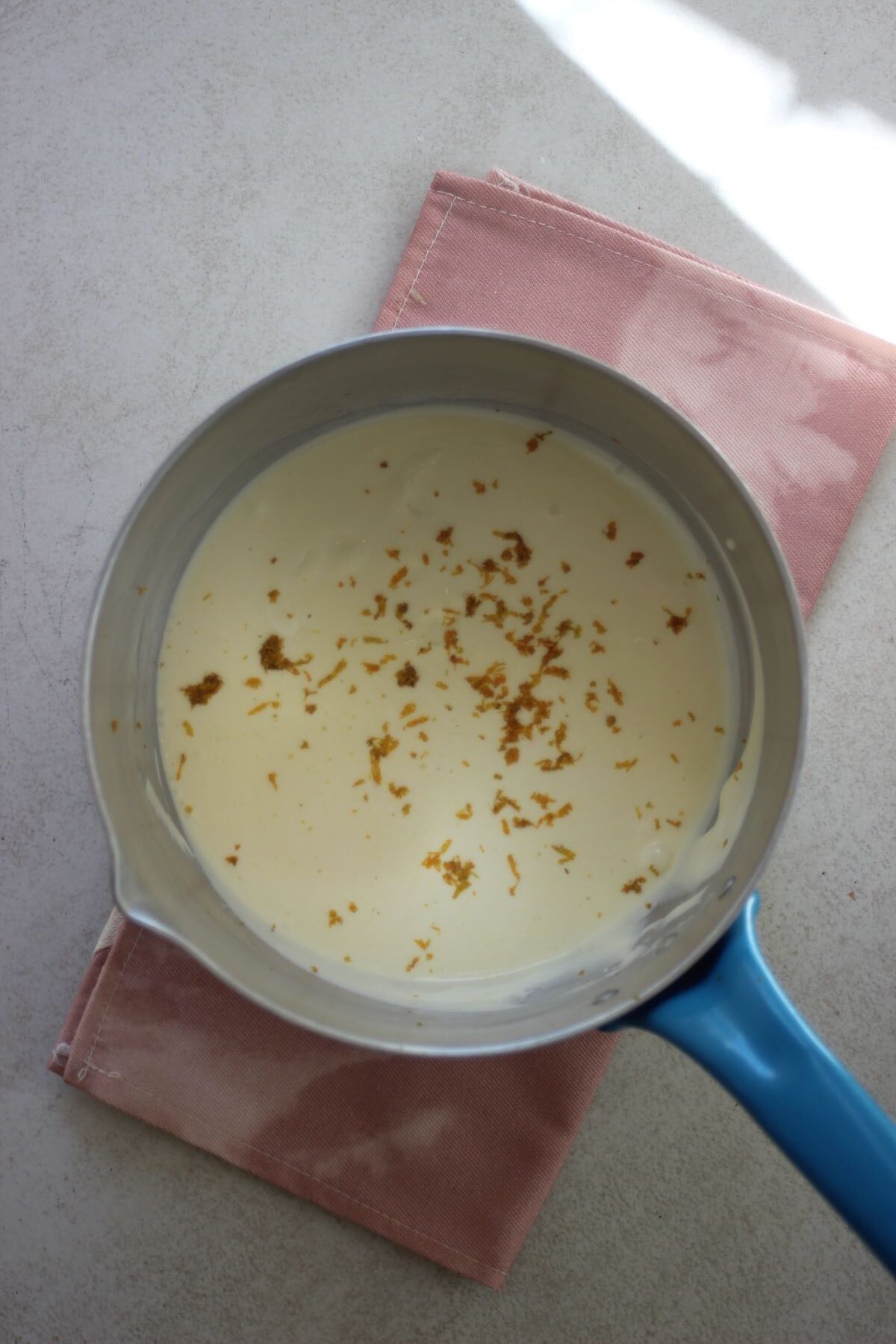 A deep saucepan with a white liquid and orange zest.