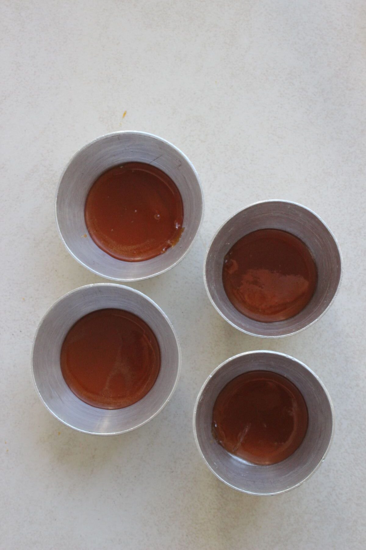 Four flan molds with caramel on a white surface seen from above.