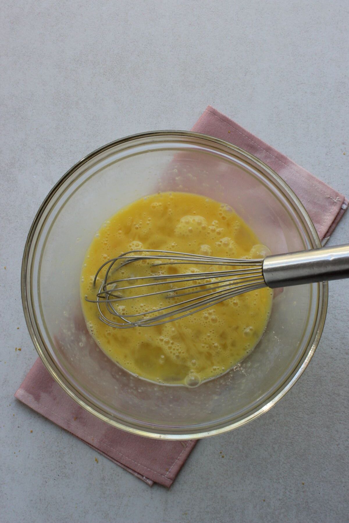 Glass bowl with eggs beaten and a hand whisk.