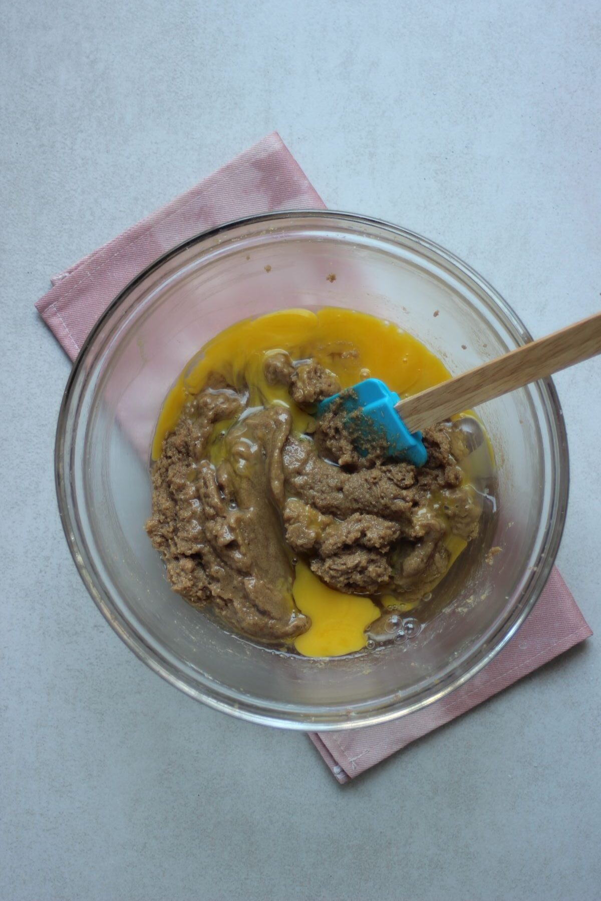 Glass bowl with egg yolks and whites,  peanut butter and a rubber spatula.