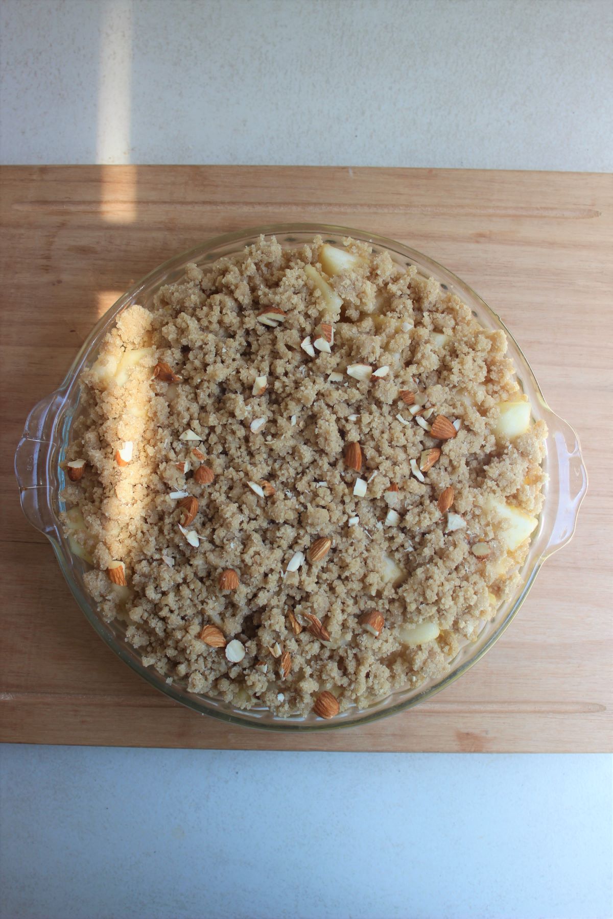 Round baking dish with pear crumble dessert on a wooden board.
