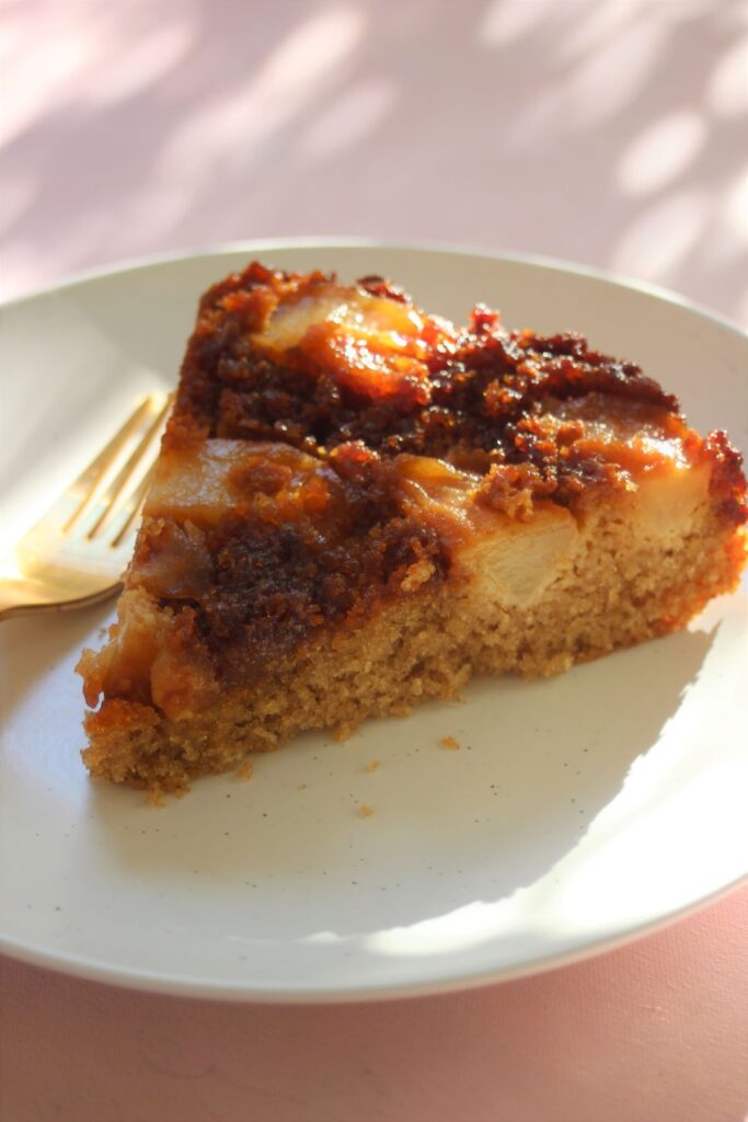 A portion of pear upside-down cake on a white plate and a golden fork.