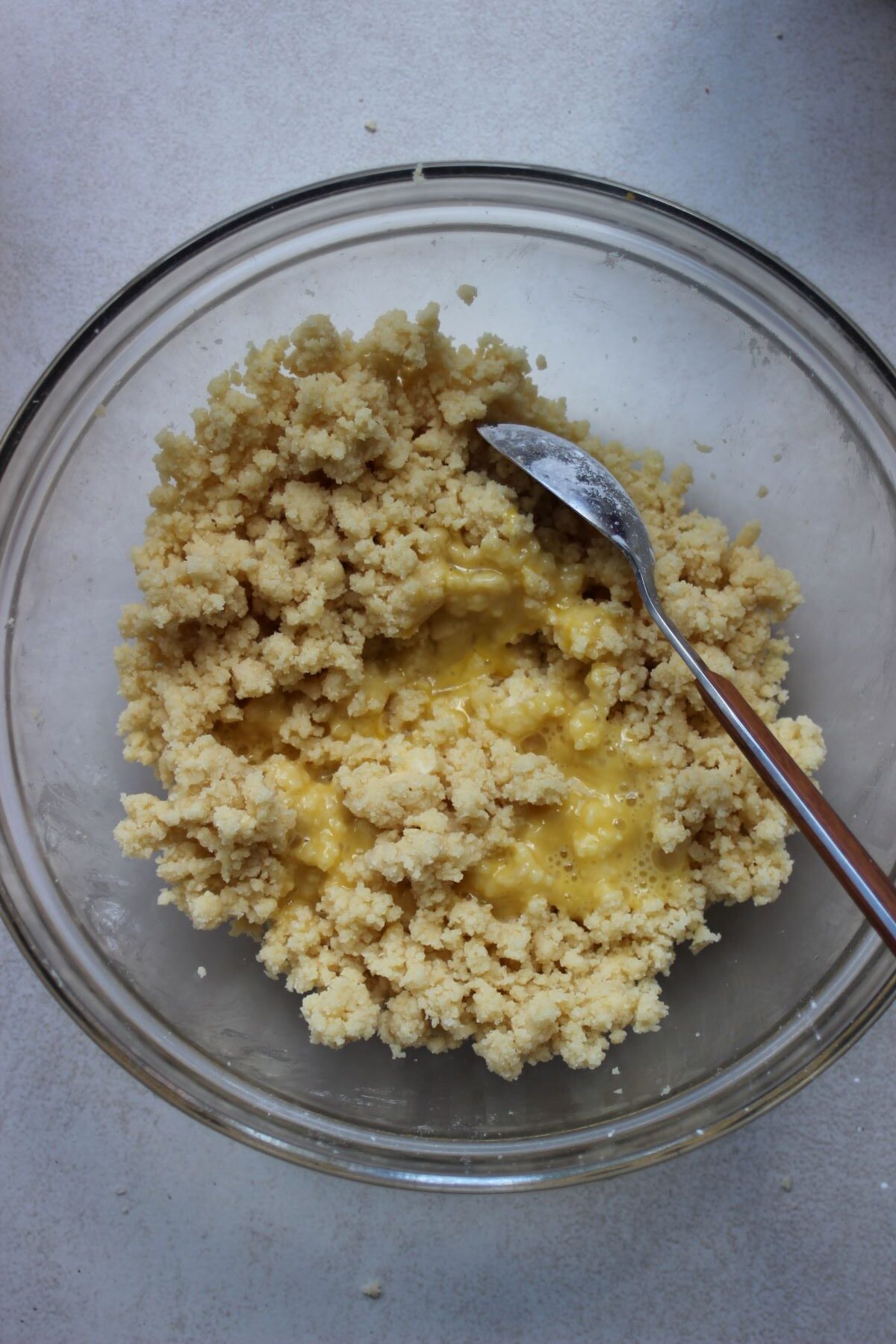 Glass bowl with dough crumbs, egg yolks and a spoon.