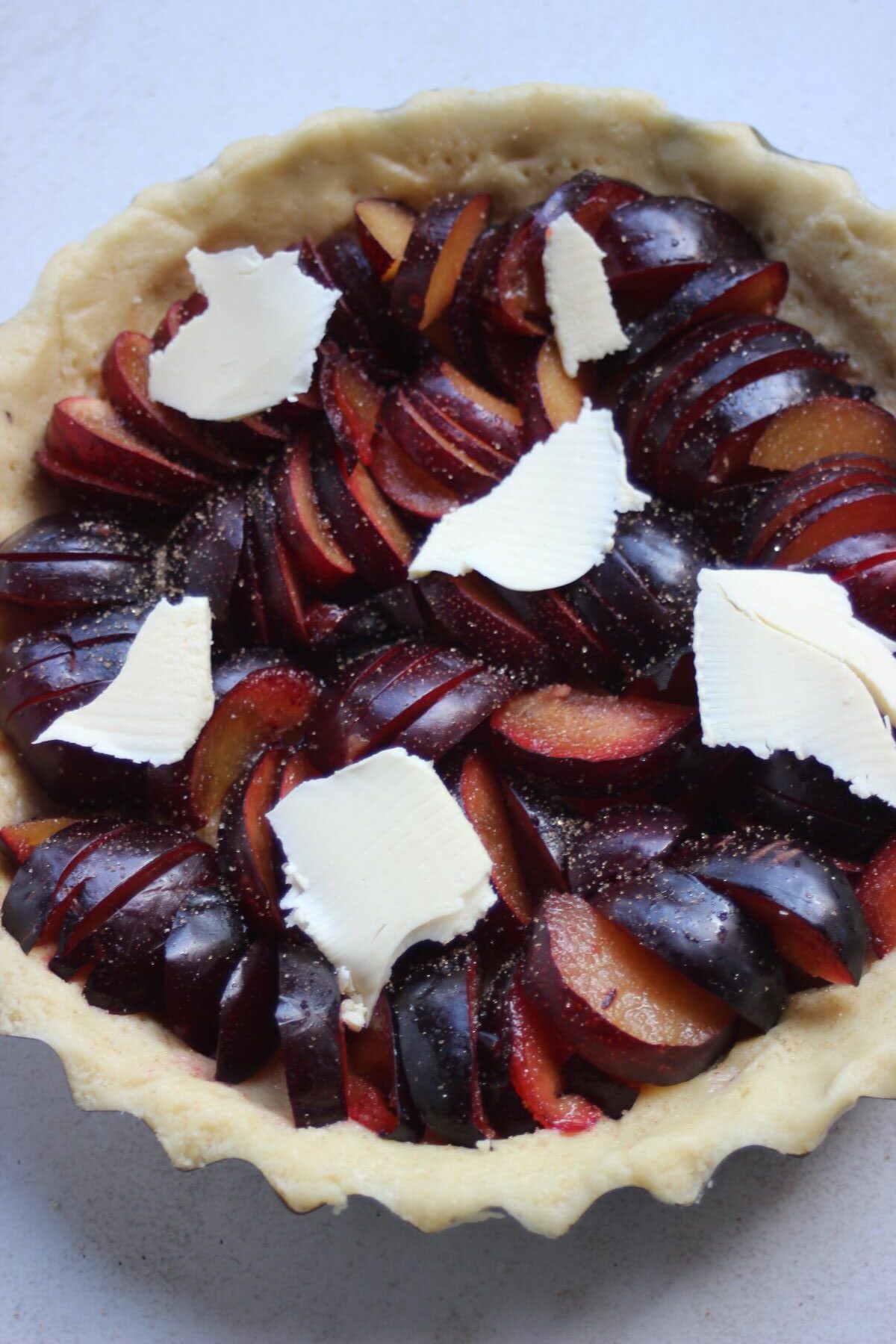 Plum tart before bake with pieces of butter on the top seen from above.