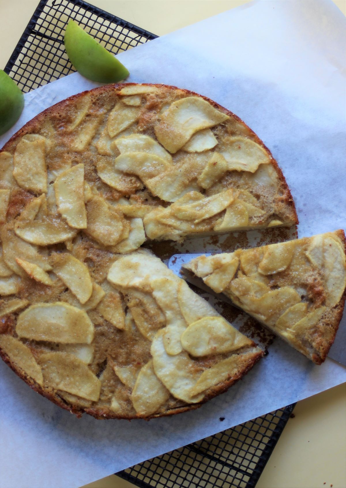 Apple cake on a parchment paper seen from above. A portion coming out of the cake.