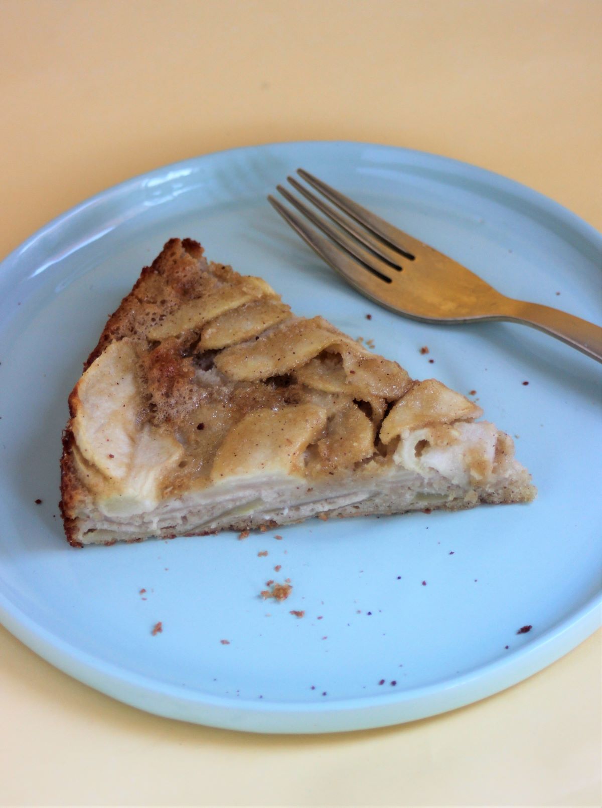 A portion of apple cake on a light blue plate and a golden fork.