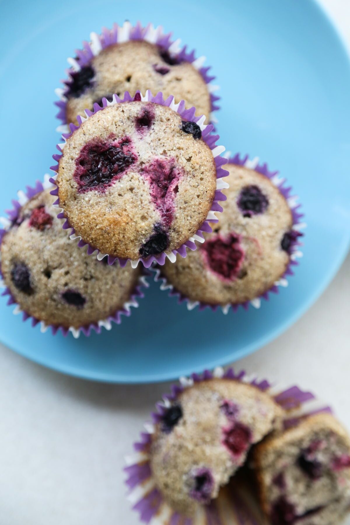 Mixed berry muffins with liners on a light blue plate seen from above.