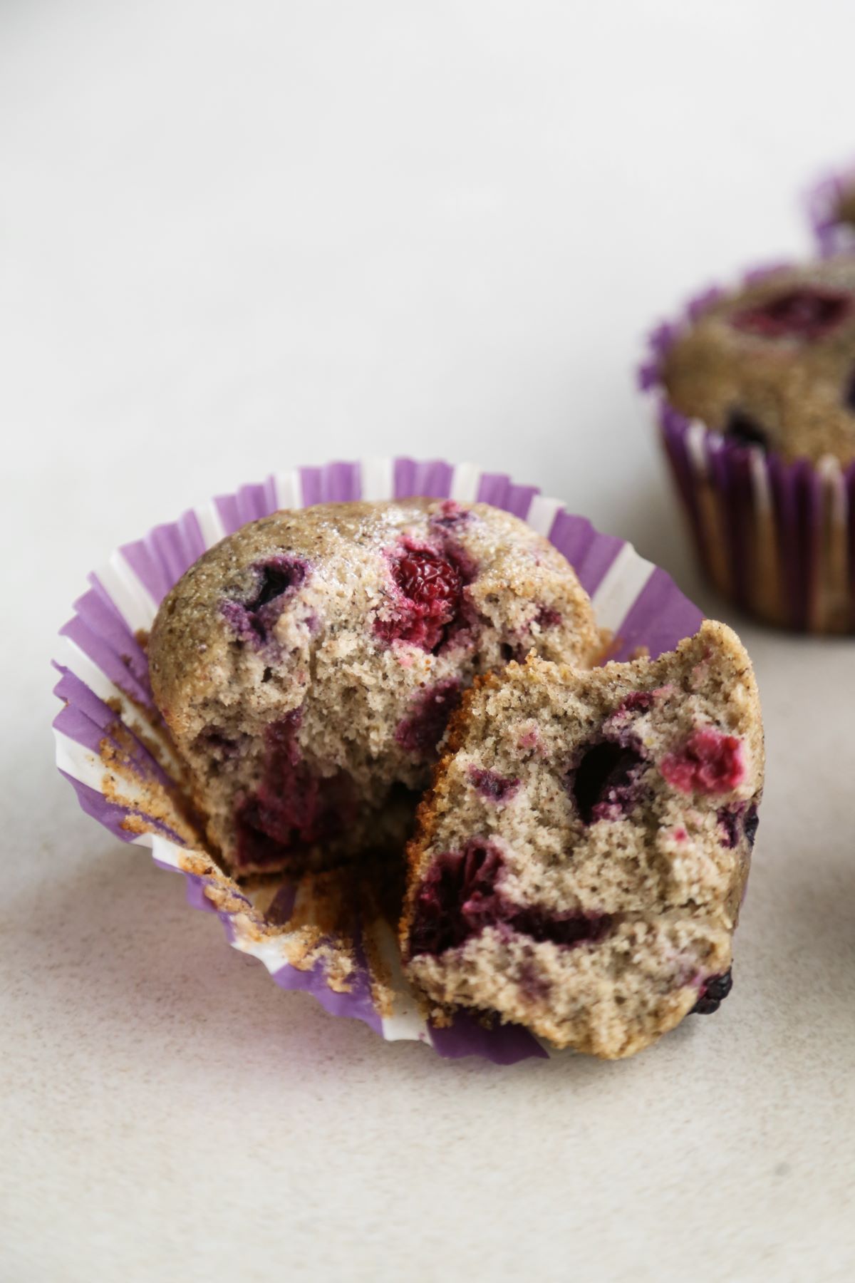A muffin with mixed berry cut in half in a liner on a white surface.