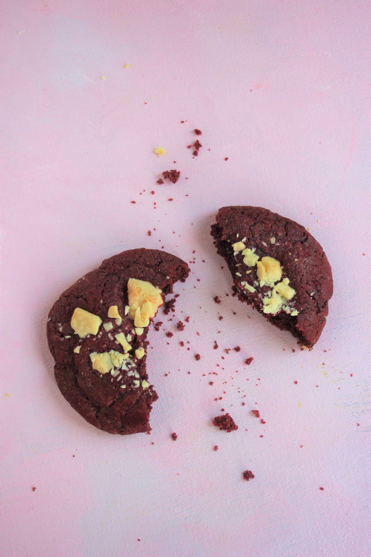 Red velvet cookie with white chocolate chunks, cut in half on a pink surface.