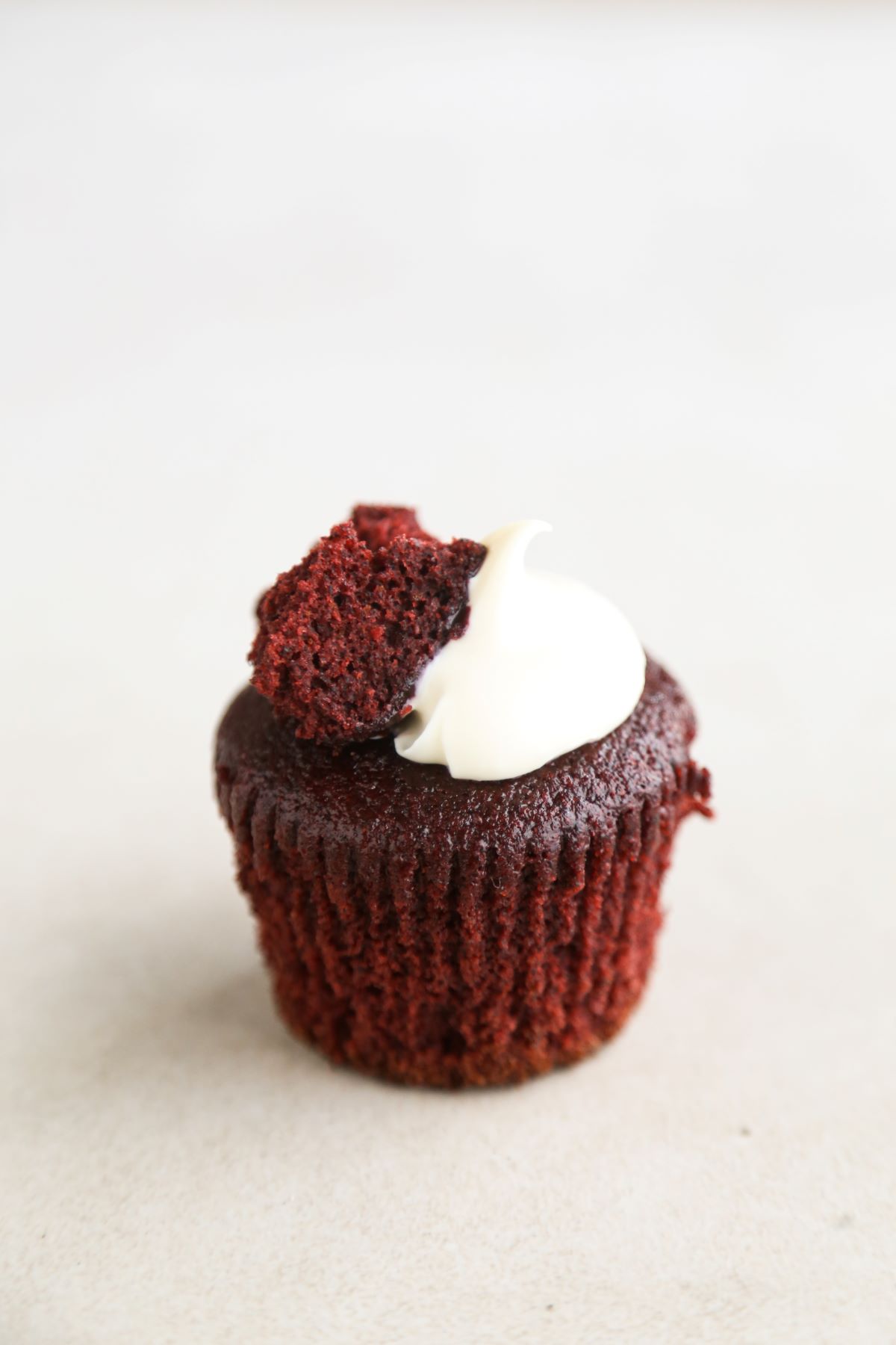 Red velvet muffin with cream cheese frosting on a white surface.