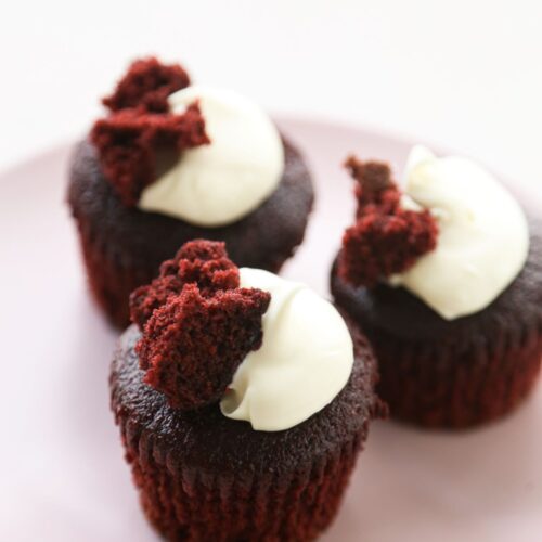 Red velvet muffins with cream cheese frosting on a pink plate.