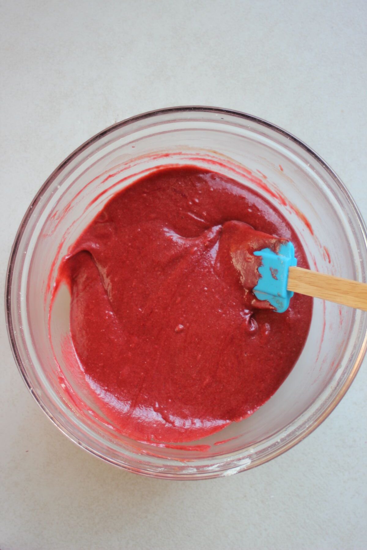 Glass bowl with a red mixture and a rubber spatula.